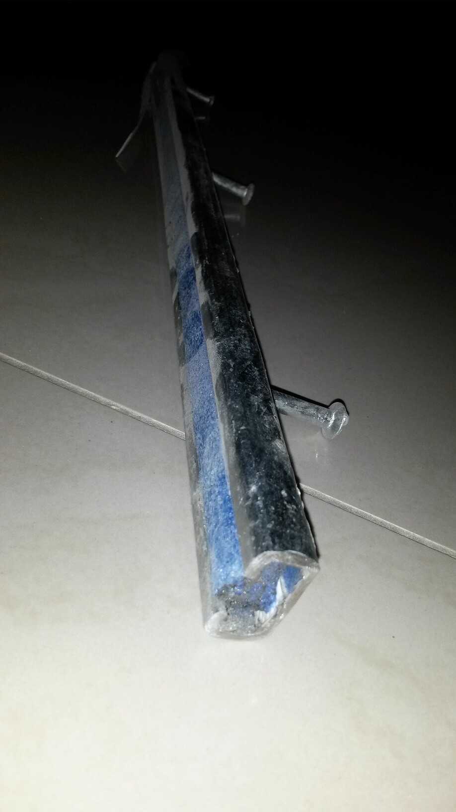 Langes Metallprofil mit Bolzen liegt auf hellen Bodenfliesen im dunklen Hintergrund