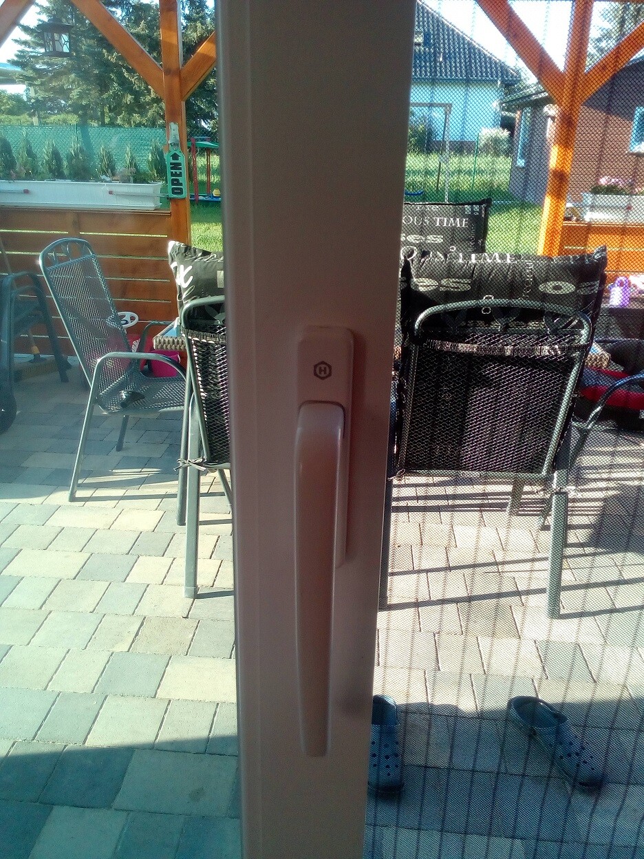 Blick durch Glas-Tür auf Terrasse mit Stühlen und Garten im Hintergrund