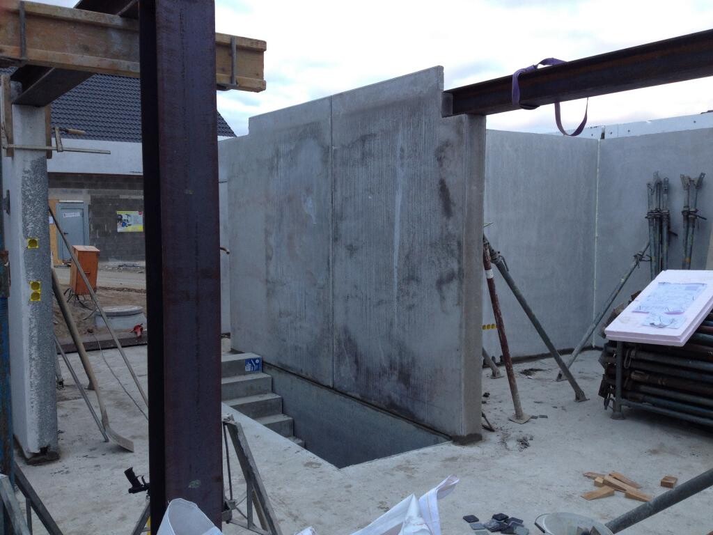 Baustelle mit grauen Betonwänden, Stahlträgern, Gerüsten und Bauplänen.