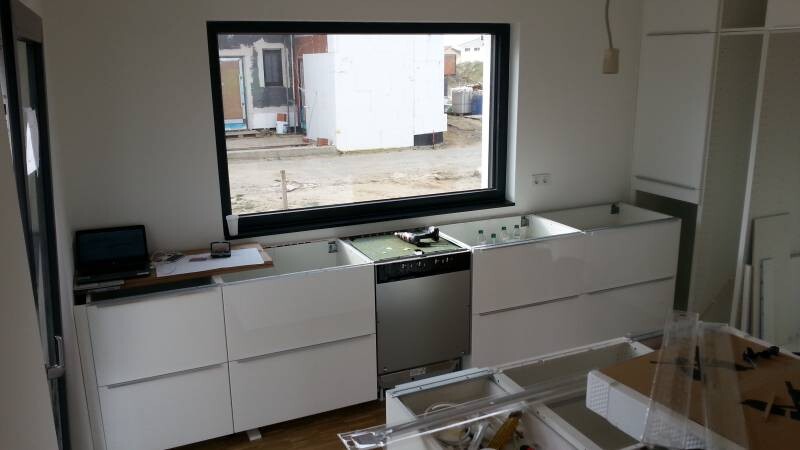 Moderne weiße Einbauküche mit Spülmaschine in der Mitte, großem Fenster und Baustelle außerhalb.