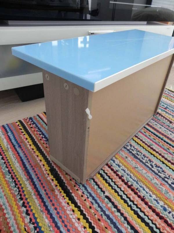 Kücheninsel mit blauem Deckel und Holzfront auf buntem Teppichboden.