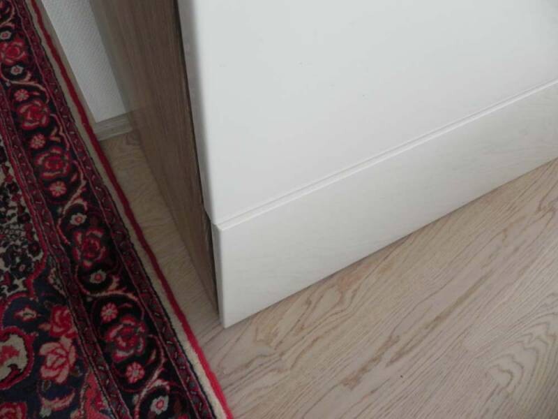 Weiße Möbelkante am Holzfußboden, linker roter Teppichrand sichtbar.