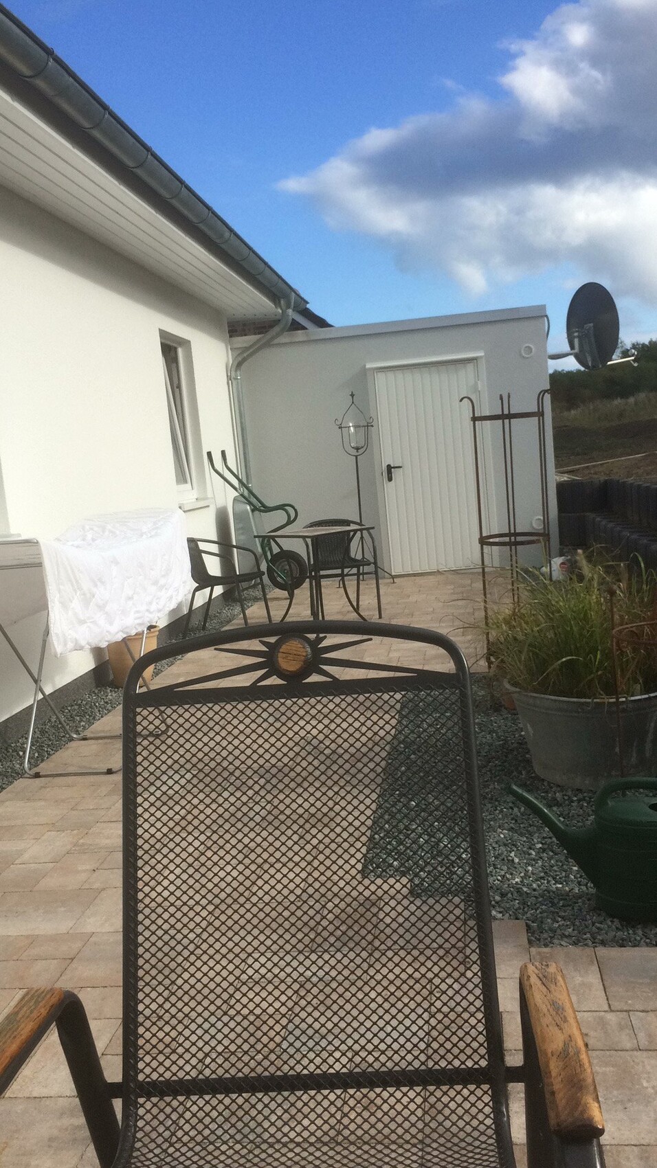 Terrasse mit Metallmöbeln, Gartenbereich vor weißer Hauswand