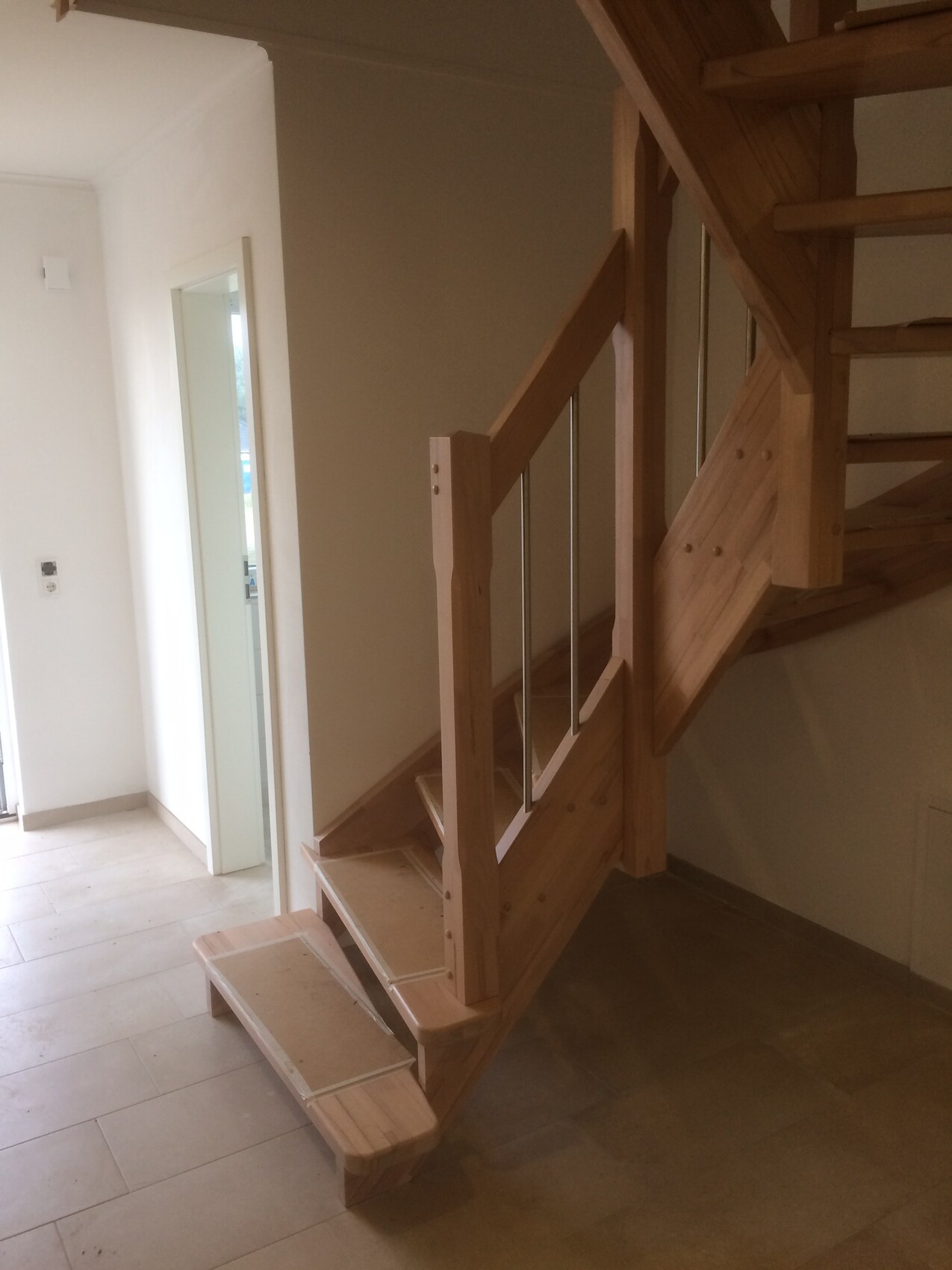 Holztreppe im Innenraum mit Geländer aus Metallstäben, linke Tür sichtbar.