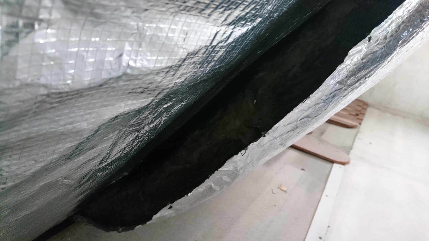 Nahaufnahme einer Aluminium-Dämmfolie mit Spalte und dunklem Hohlraum dahinter.