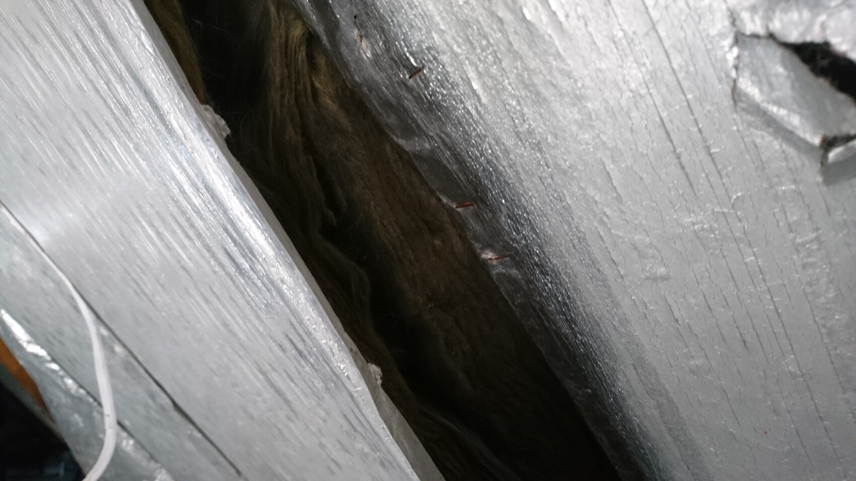 Nahaufnahme von grau gestrichenem Holz mit Spalte, dunkler Hohlraum dahinter.