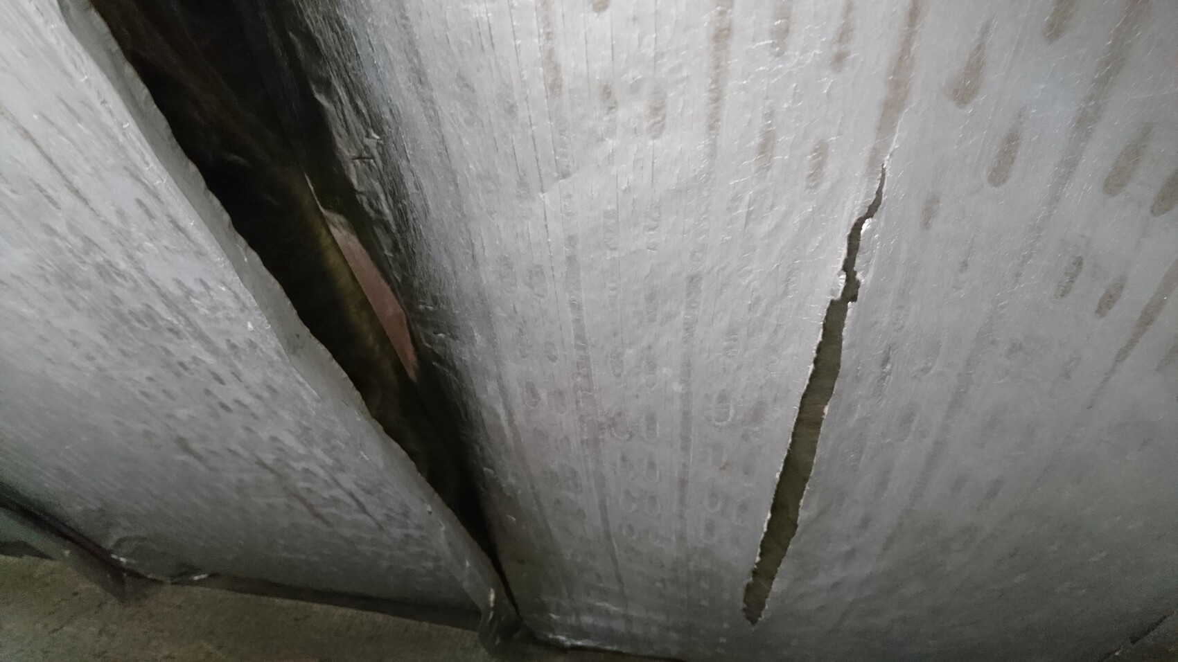 Großer vertikaler Riss in grauer Betonwand mit dunklem Spalt und rauer Oberfläche