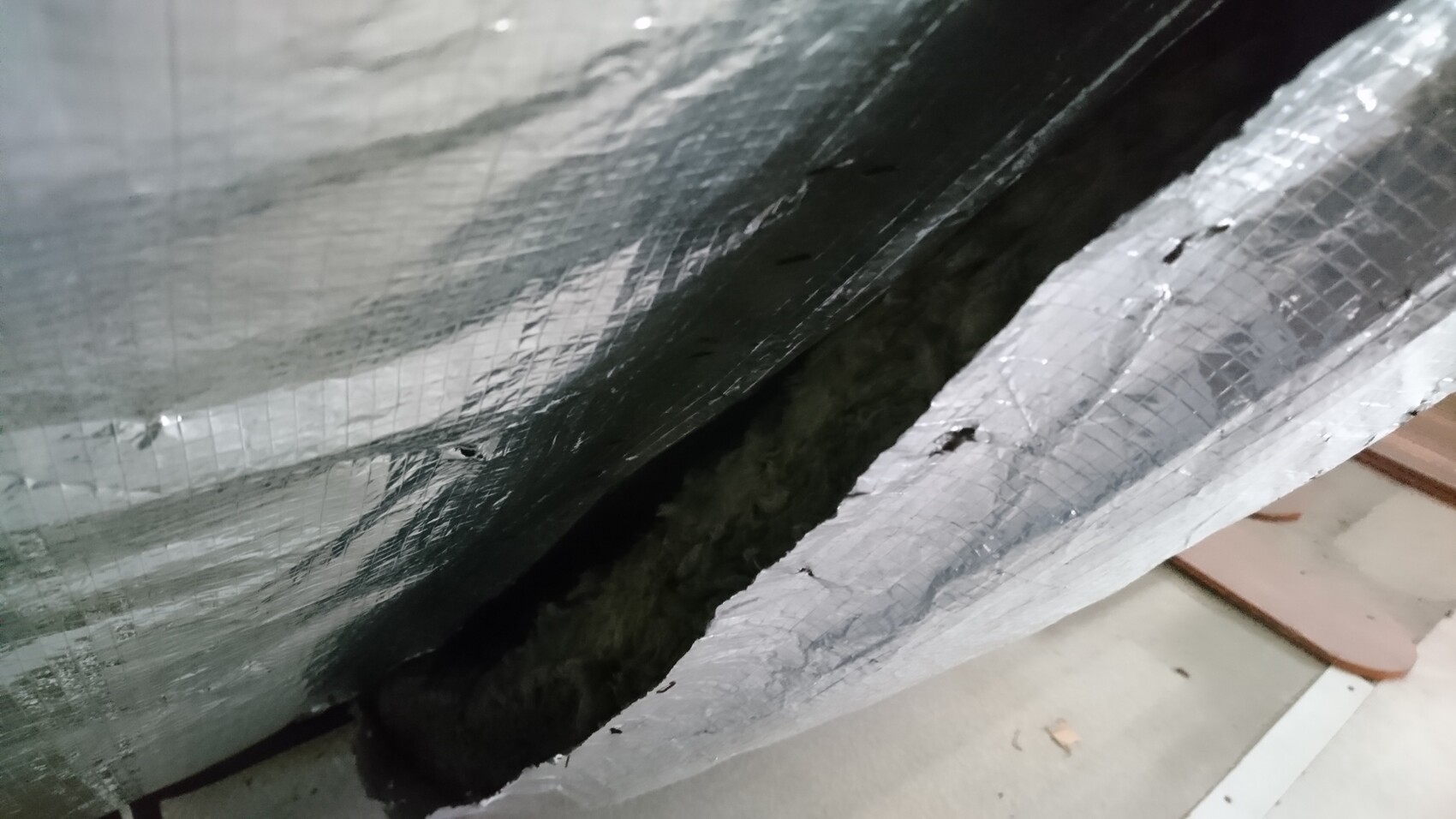 Nahaufnahme einer silbernen Isolierfolie mit Rissen, darunter eine dunkle Spalte.