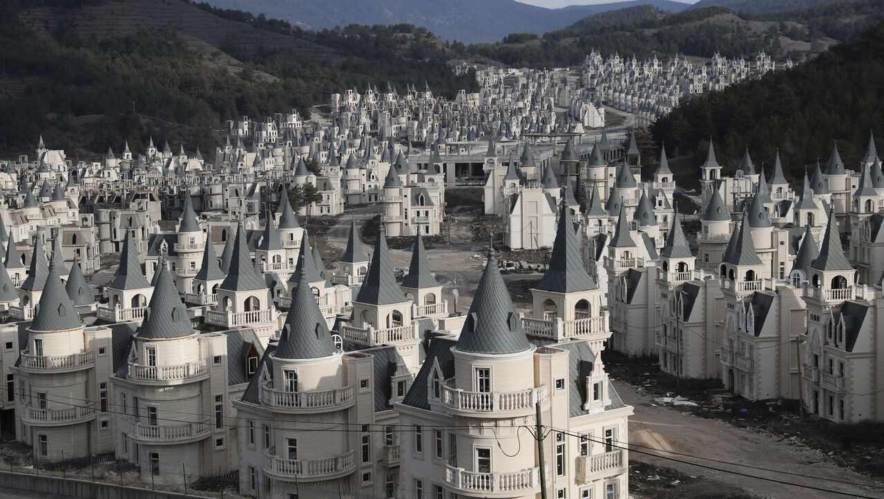 Viele weiße Schlossgebäude mit grauen spitzen Türmen in einer bergigen Landschaft