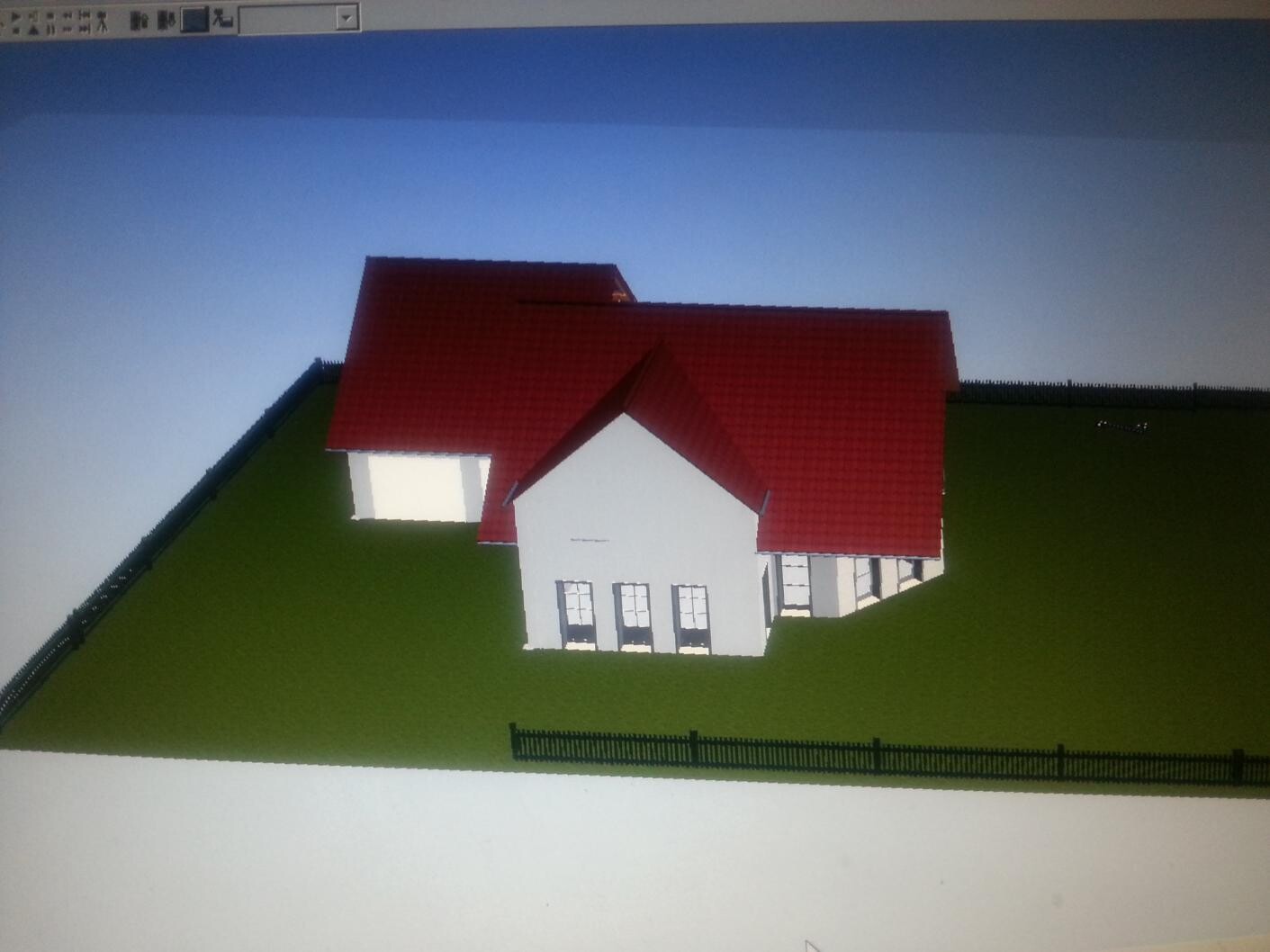3D-Architekturmodell eines weißen Hauses mit rotem Dach auf grünem Hang, Zaun im Vordergrund.