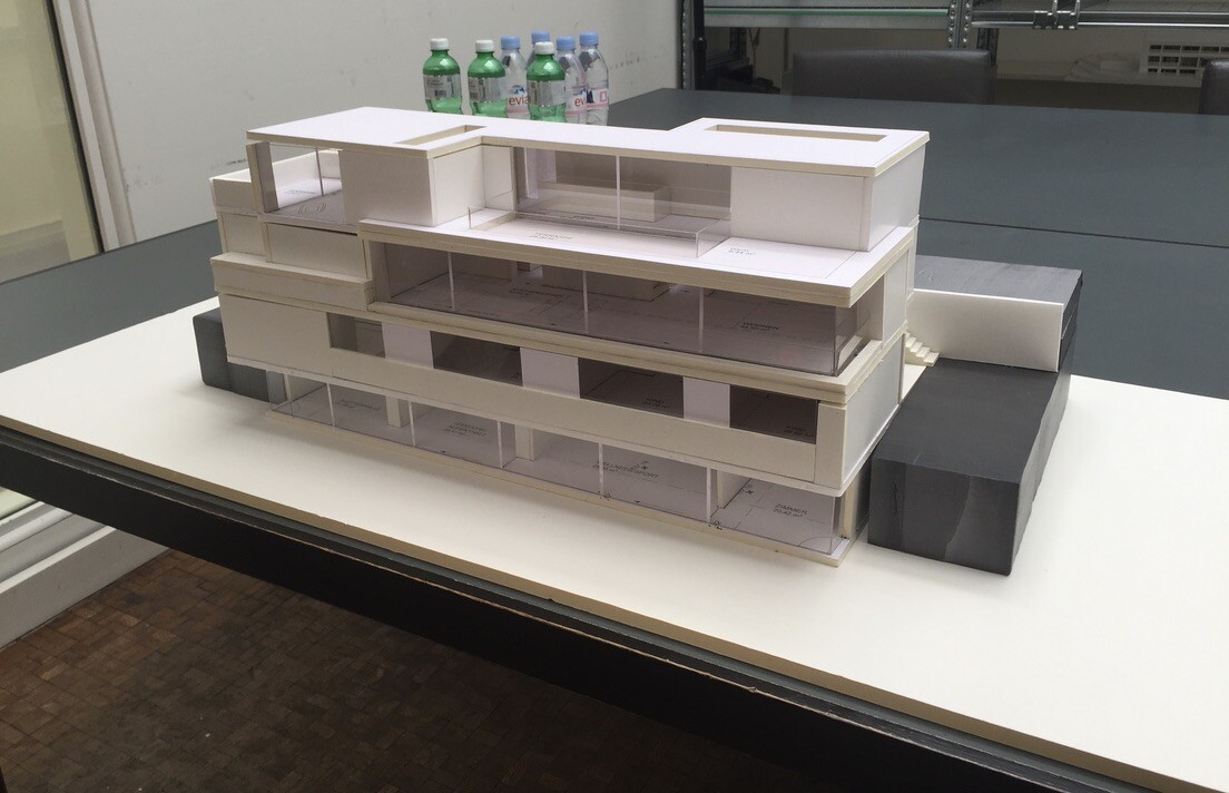 Architekturmodell eines modernen, mehrstöckigen weißen Gebäudes mit Glasfassaden.