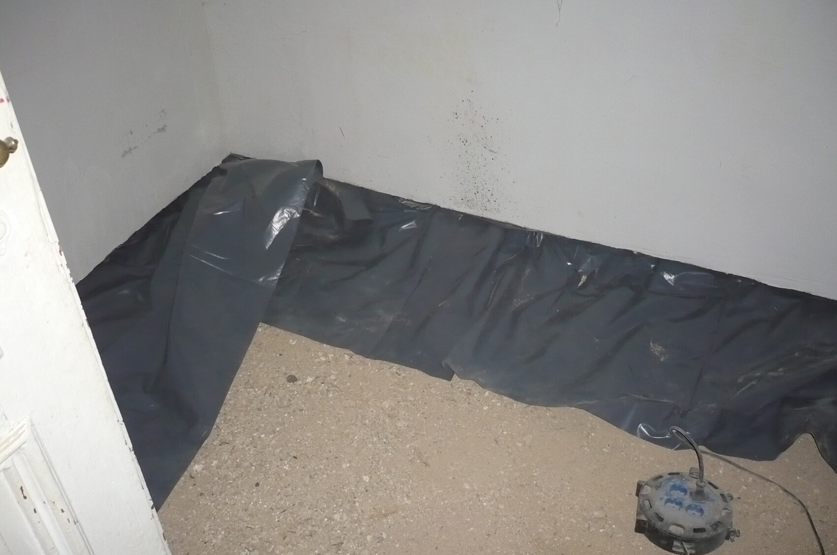 Raumecke: schwarze Plastikabdeckung liegt auf dem Boden, neben einem Schleifgerät mit Kabel.