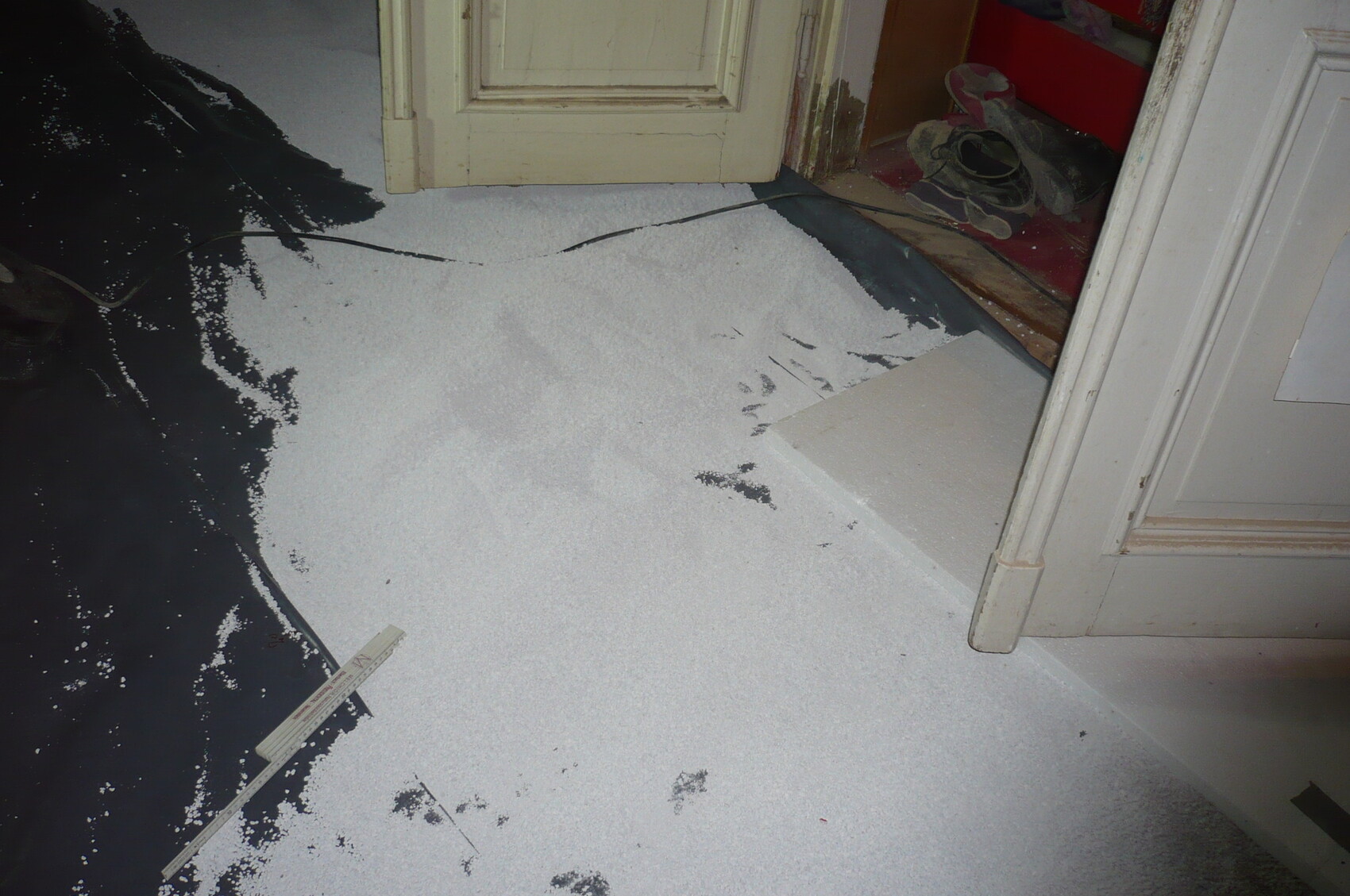 Große Menge weißes Granulat liegt als Pulver auf dem Boden, Türöffnung und Schuhe im Flur.