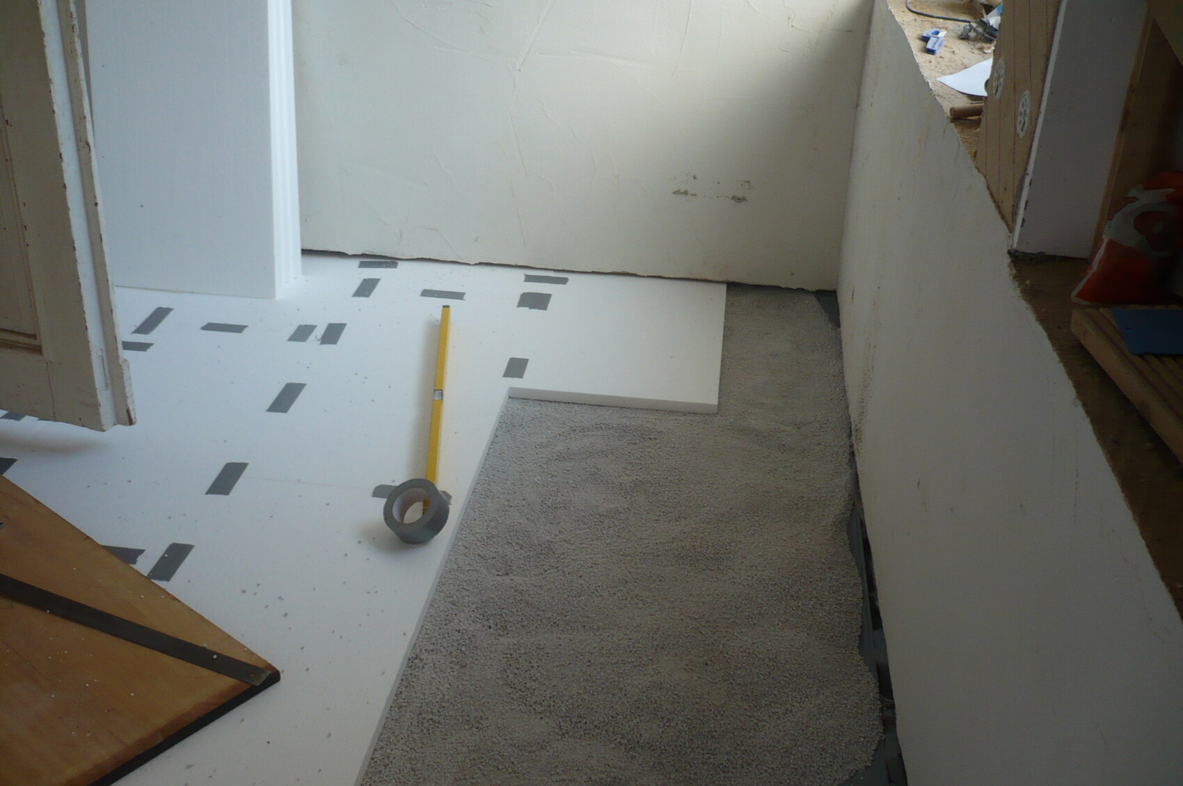 Renovierungsraum: weiße Unterbodenplatten mit schwarzem Klebeband, gelber Bleistift und Tape-Rolle.