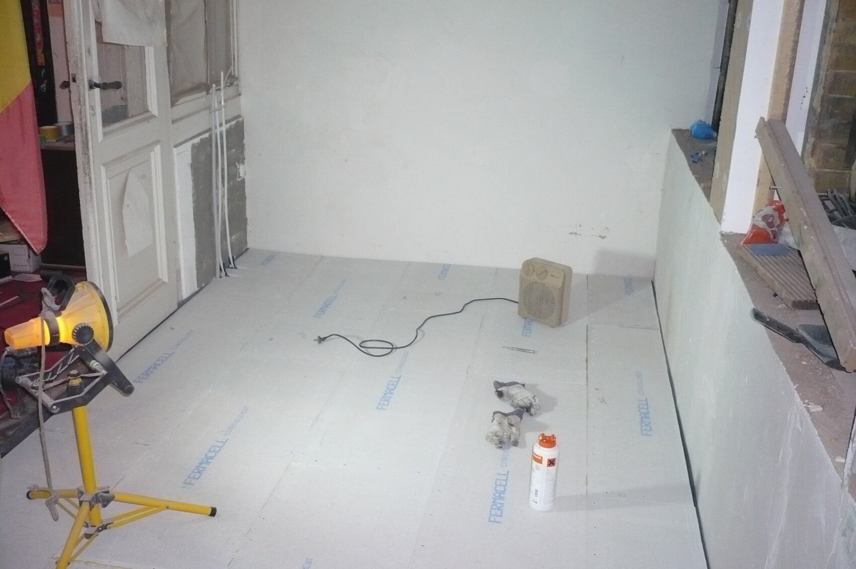 Renovierungsraum mit Dämmplatten auf dem Boden, Werkzeug, Kabel und Heizgerät.