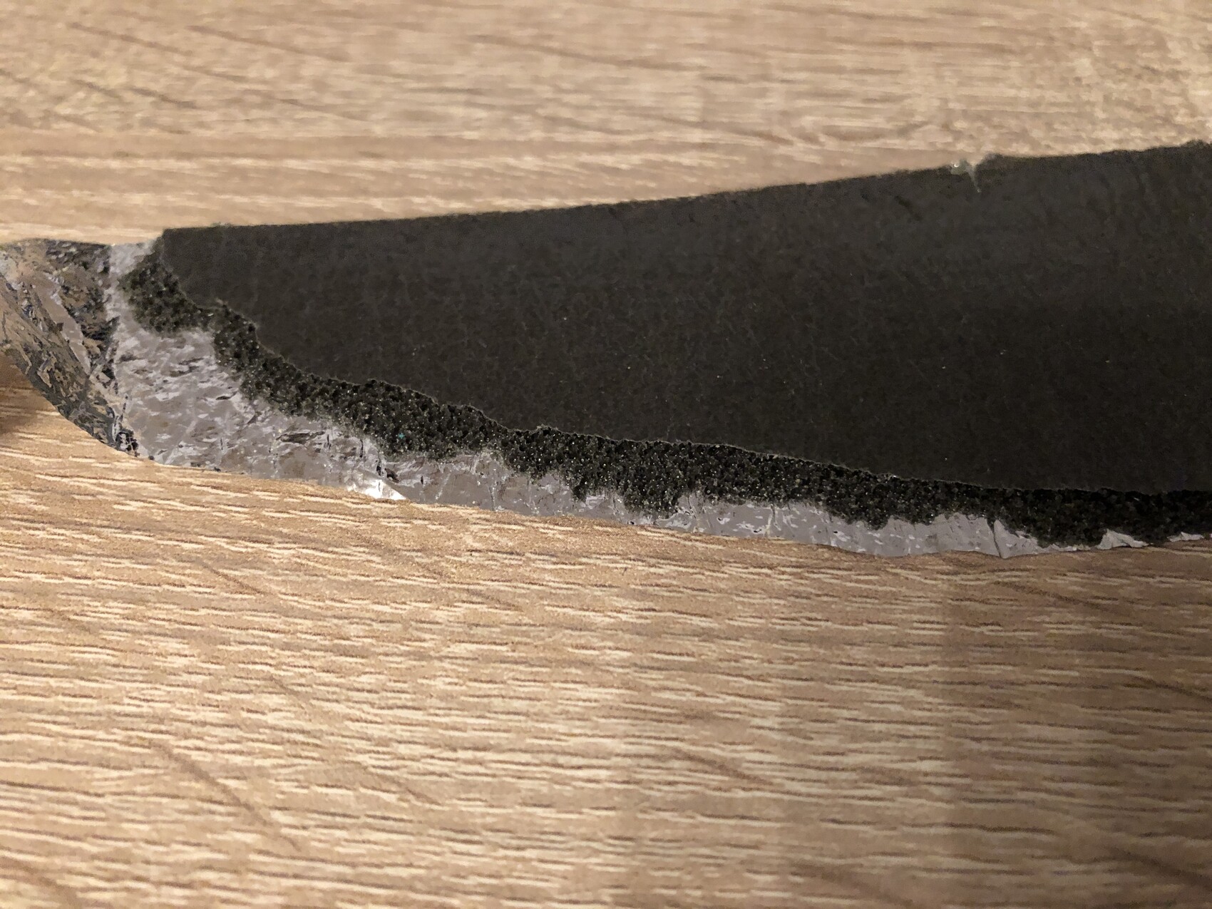 Schwarzes Dämmmaterial-Stück mit rauer Kante auf Holzunterlage, Materialprobe