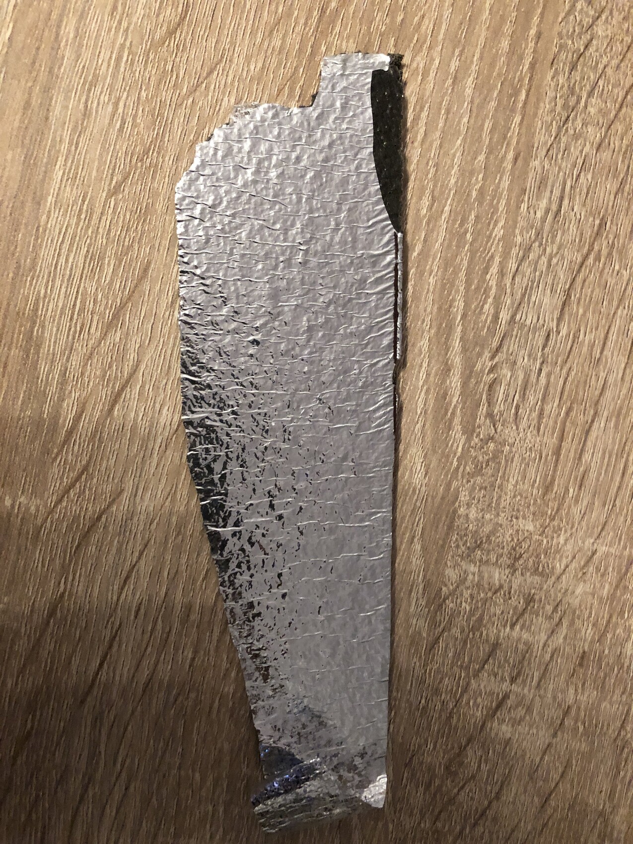 Fragment einer Aluminium-Daemmfolie auf Holzboden.