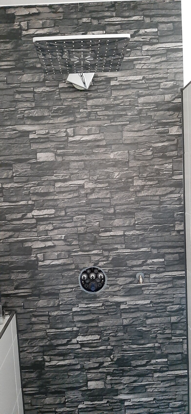 Moderne Dusche mit dunkler Steinwand, Regendusche und Armatur in Badezimmerumgebung.