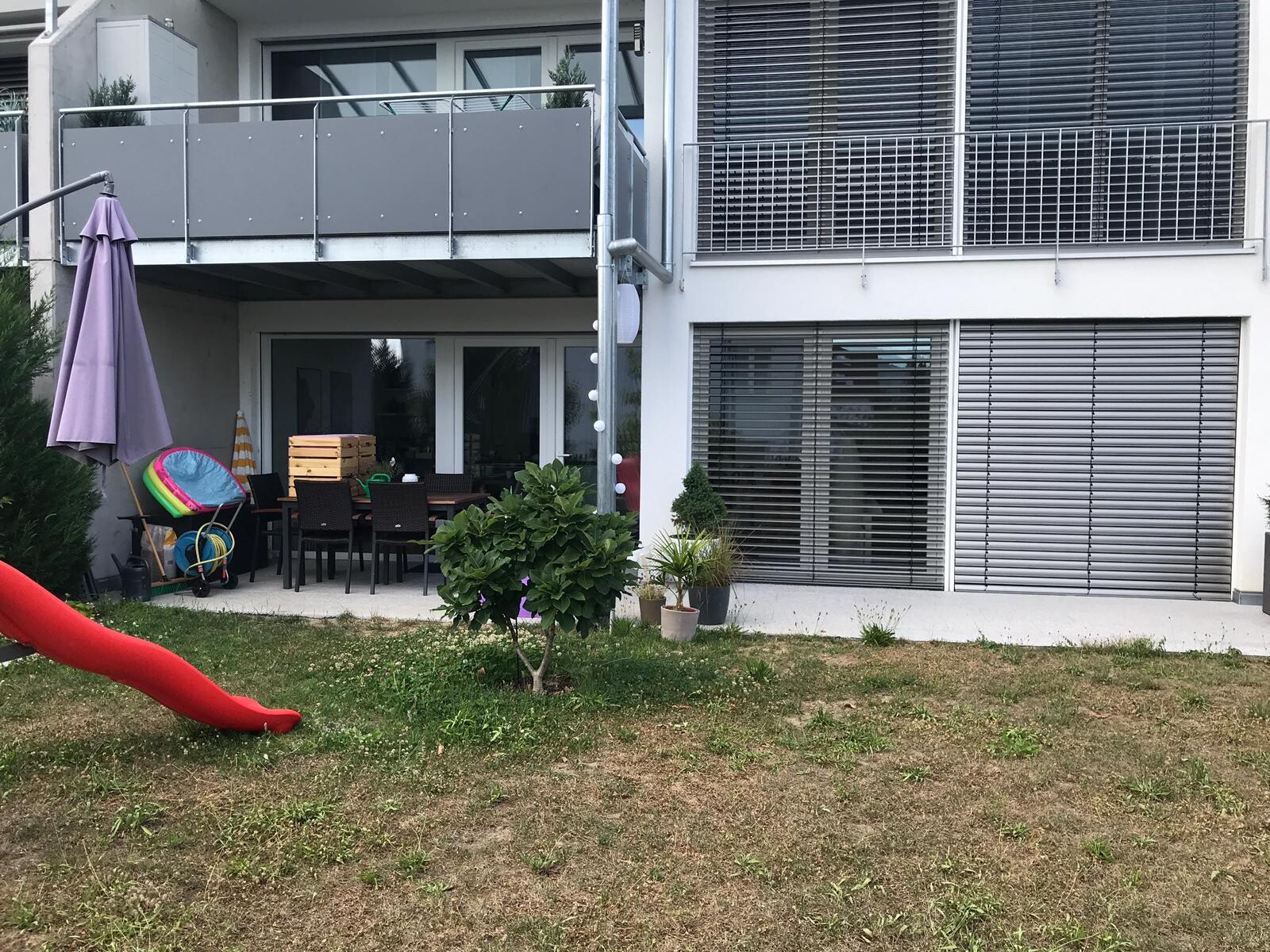 Garten-Terrasse eines Hauses mit Esstisch und Stühlen, roter Spielrutsche und Balkon darüber.