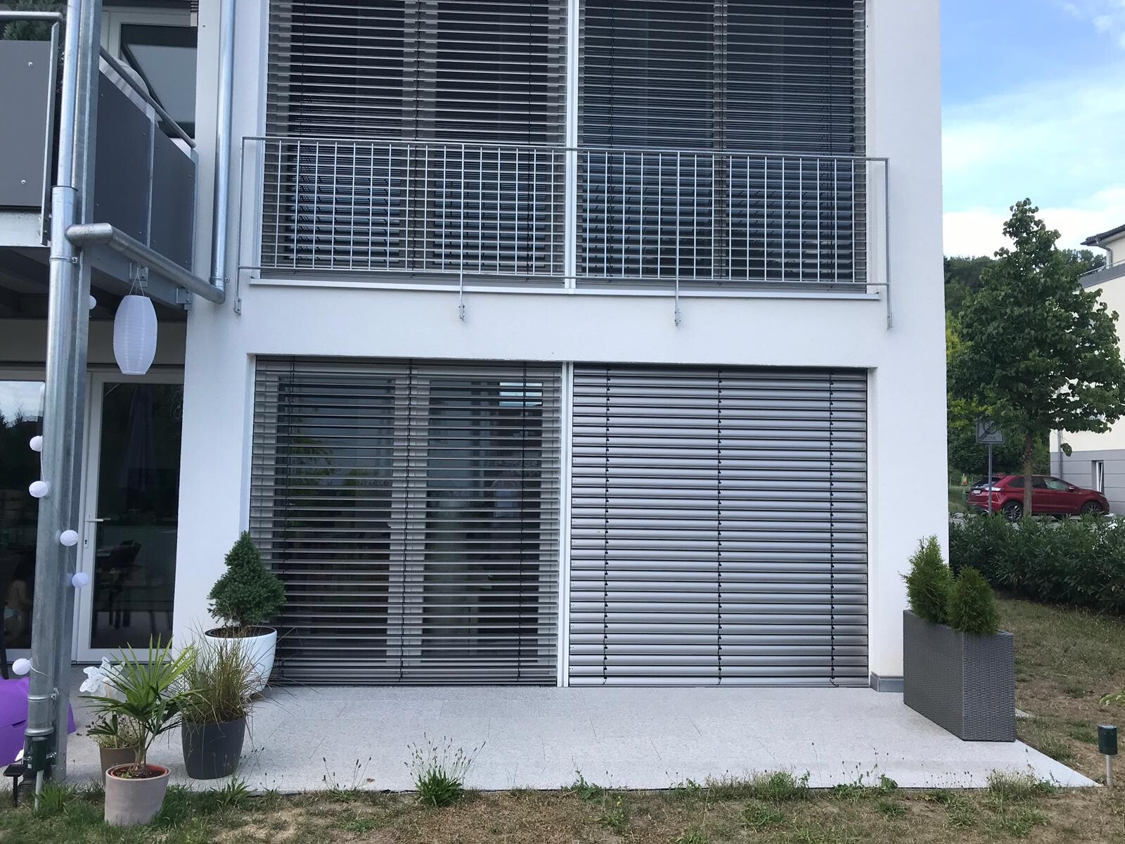 Moderne weiße Hausfassade mit großen Fenstern, Jalousien, Balkon und Lichterkette links