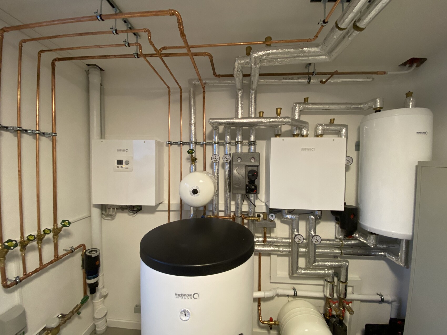 Heizungsanlage mit Rohren, Druckmessgeräten und Warmwasserspeicher im Technikraum.