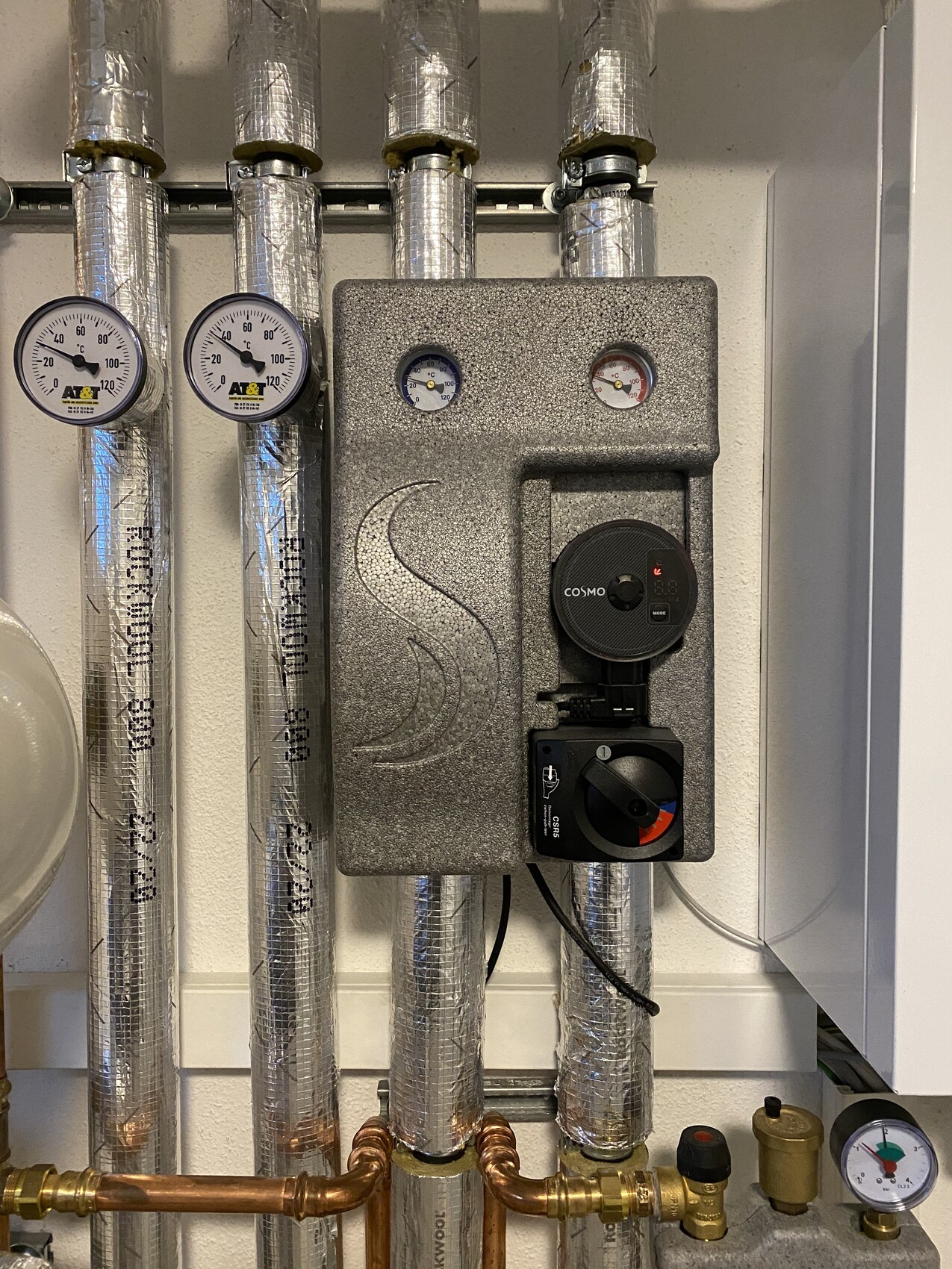 Heizungsanlage mit isolierten Rohrleitungen, zwei Temperaturmessern, Cosmo-Regler und Ventilbox.