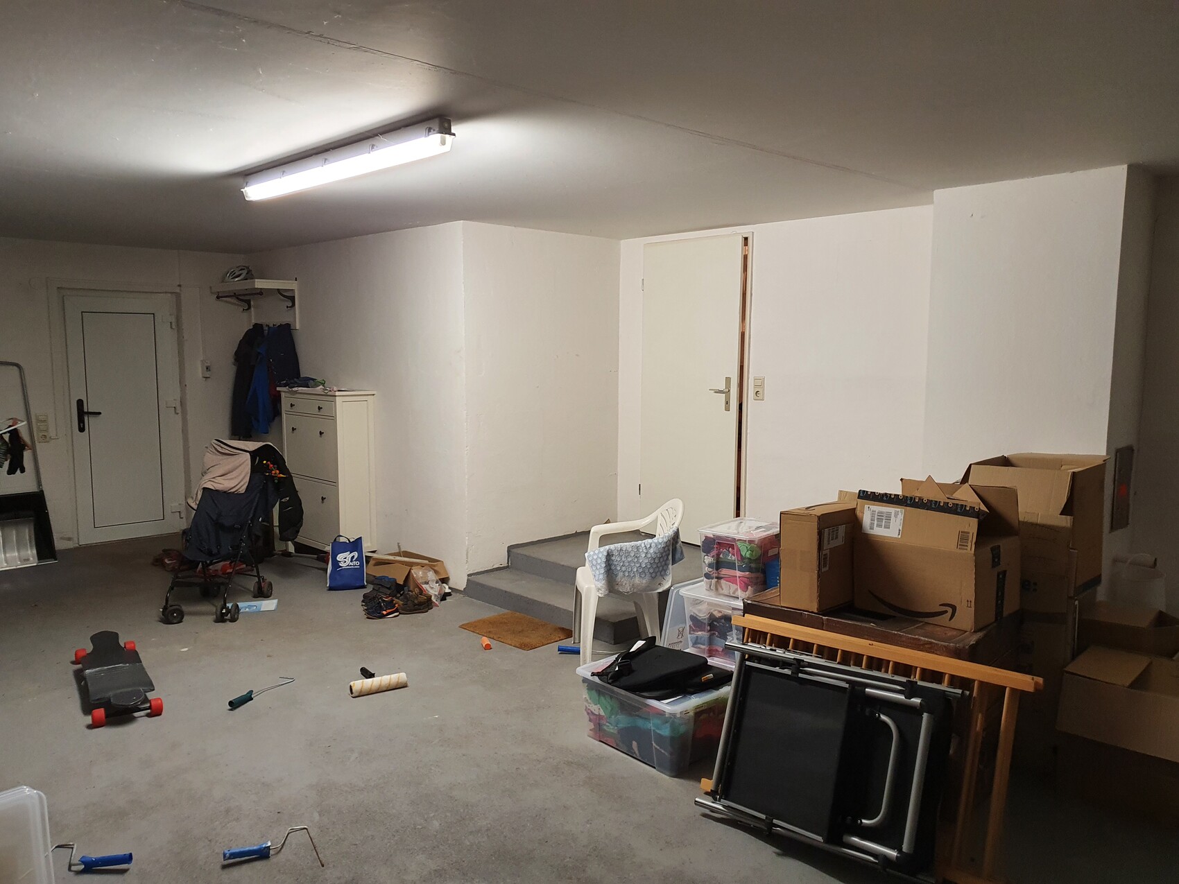 Unordentlicher Kellerraum mit Umzugskartons, Stuhl, Kinderwagen und Kleidung.