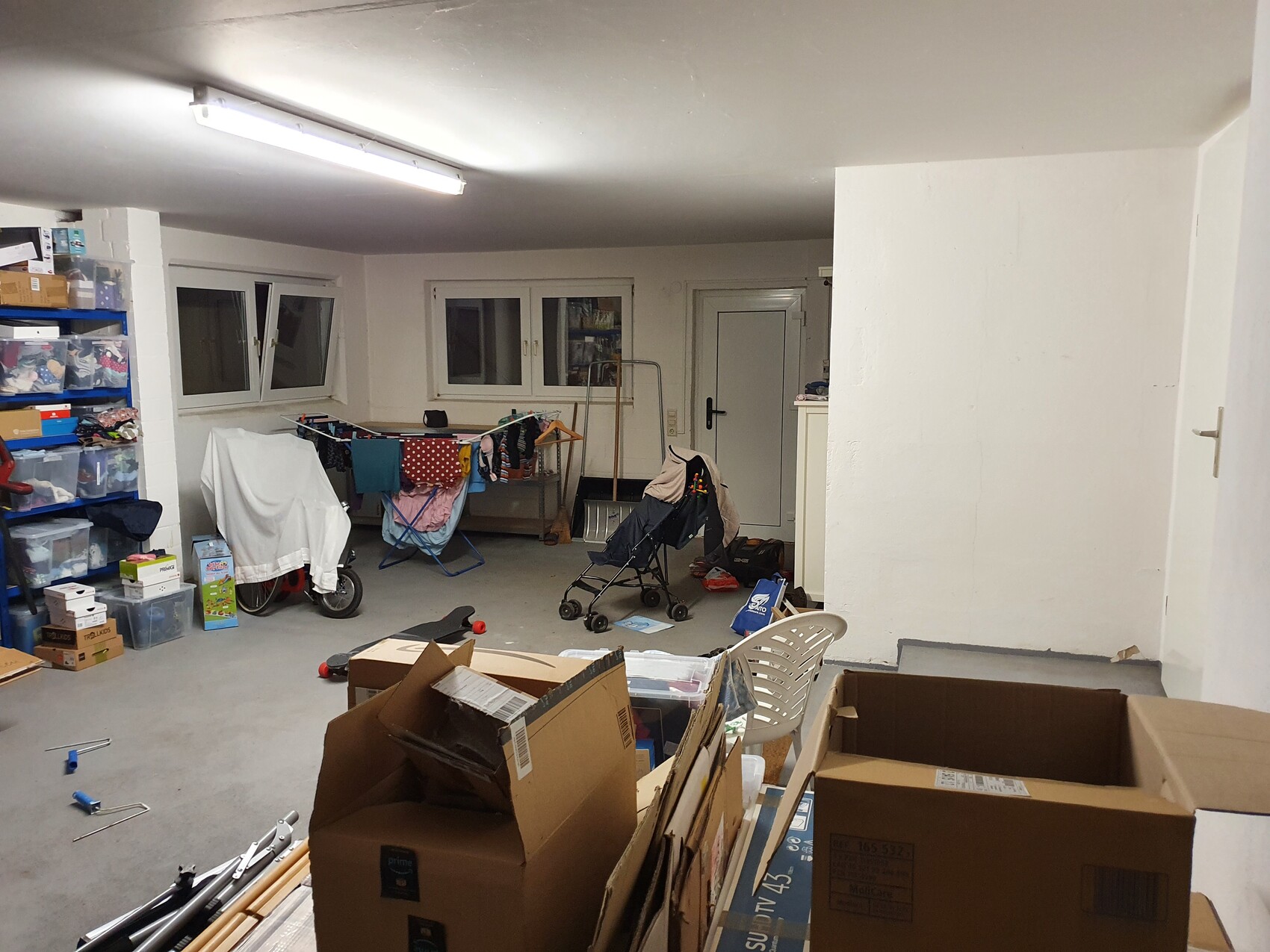 Ein unordentlicher Kellerabstellraum mit Regalen, Kartons, Wäscheleine und Kinderwagen.