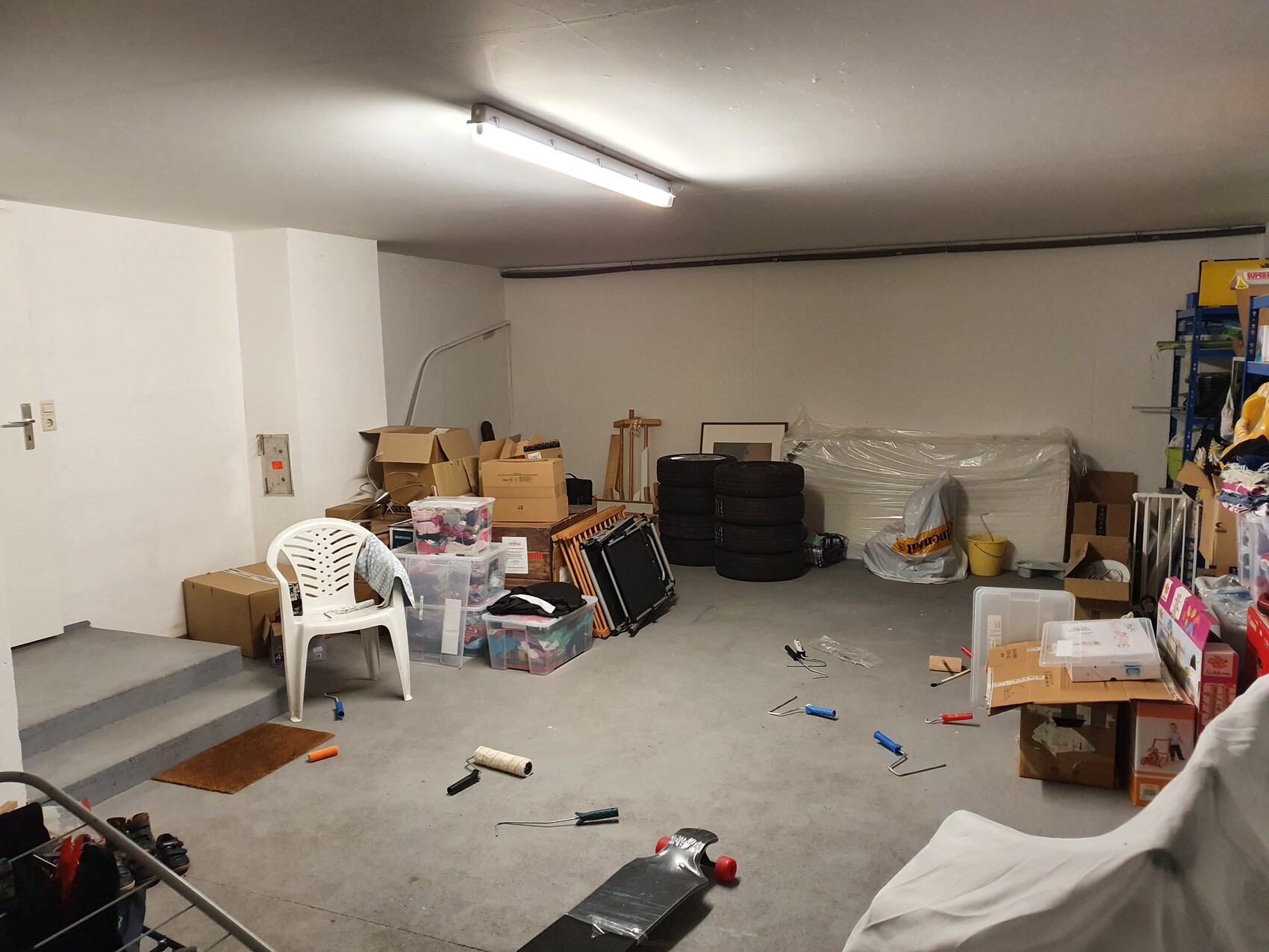Kellerabstellraum mit Kartons, Plastikkisten, Reifenstapeln, Stuhl und Werkzeugen.