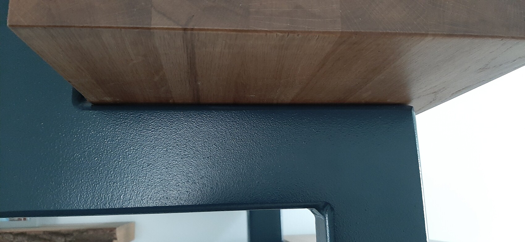 Holzbalken liegt auf dunklem Stahlrahmen; Holz- und Metalloberflächen sichtbar.