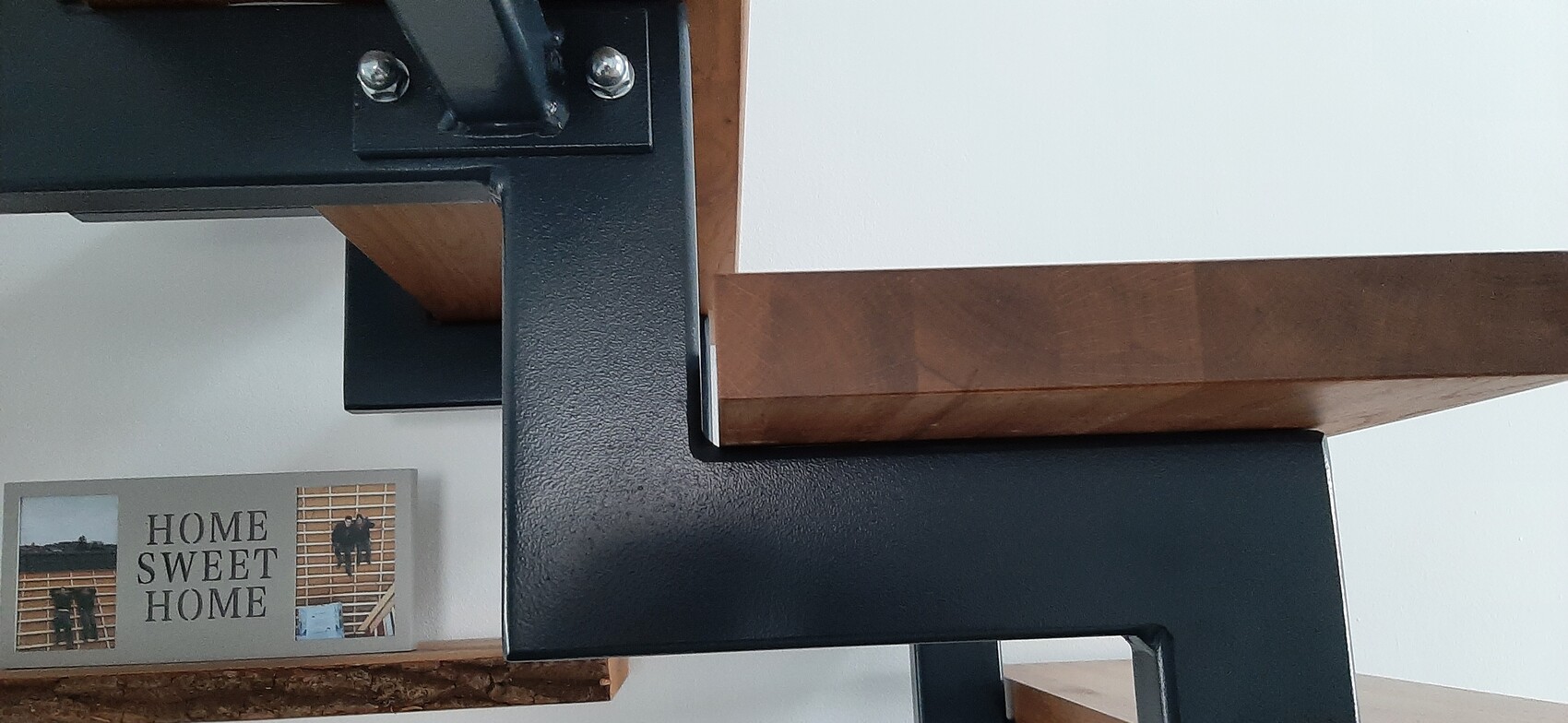 Nahaufnahme eines schwarzen Metallrahmens mit Holzplatte; links unten Schild HOME SWEET HOME.