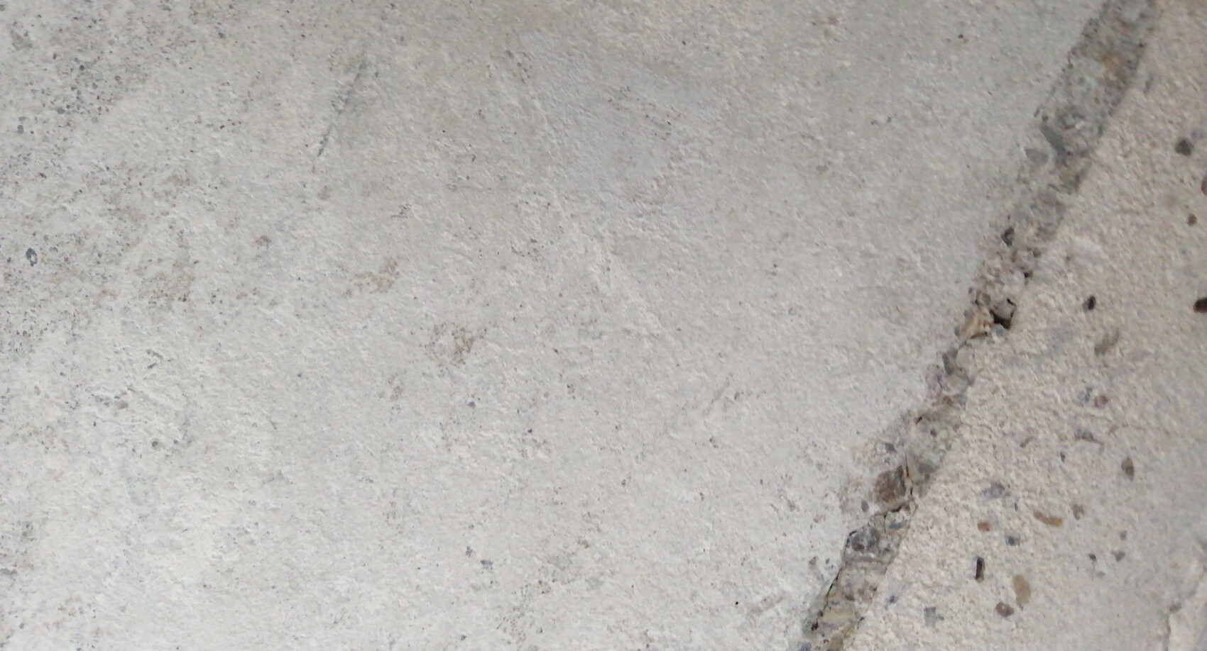 Nahaufnahme einer rauen Betonfläche mit einer schmalen Risslinie am rechten Rand.
