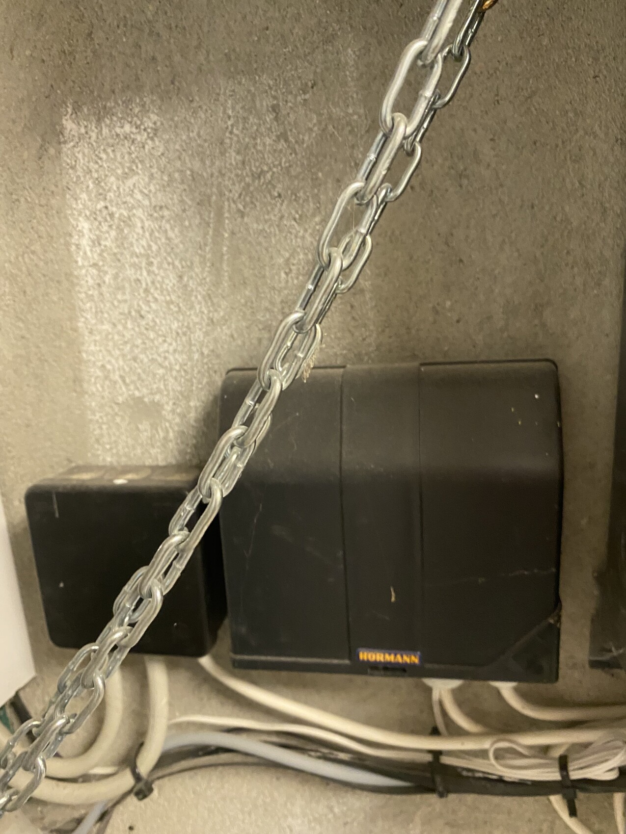 Schwarzer Hörmann-Garagenantrieb an Betonwand, davor liegt eine Metallkette.