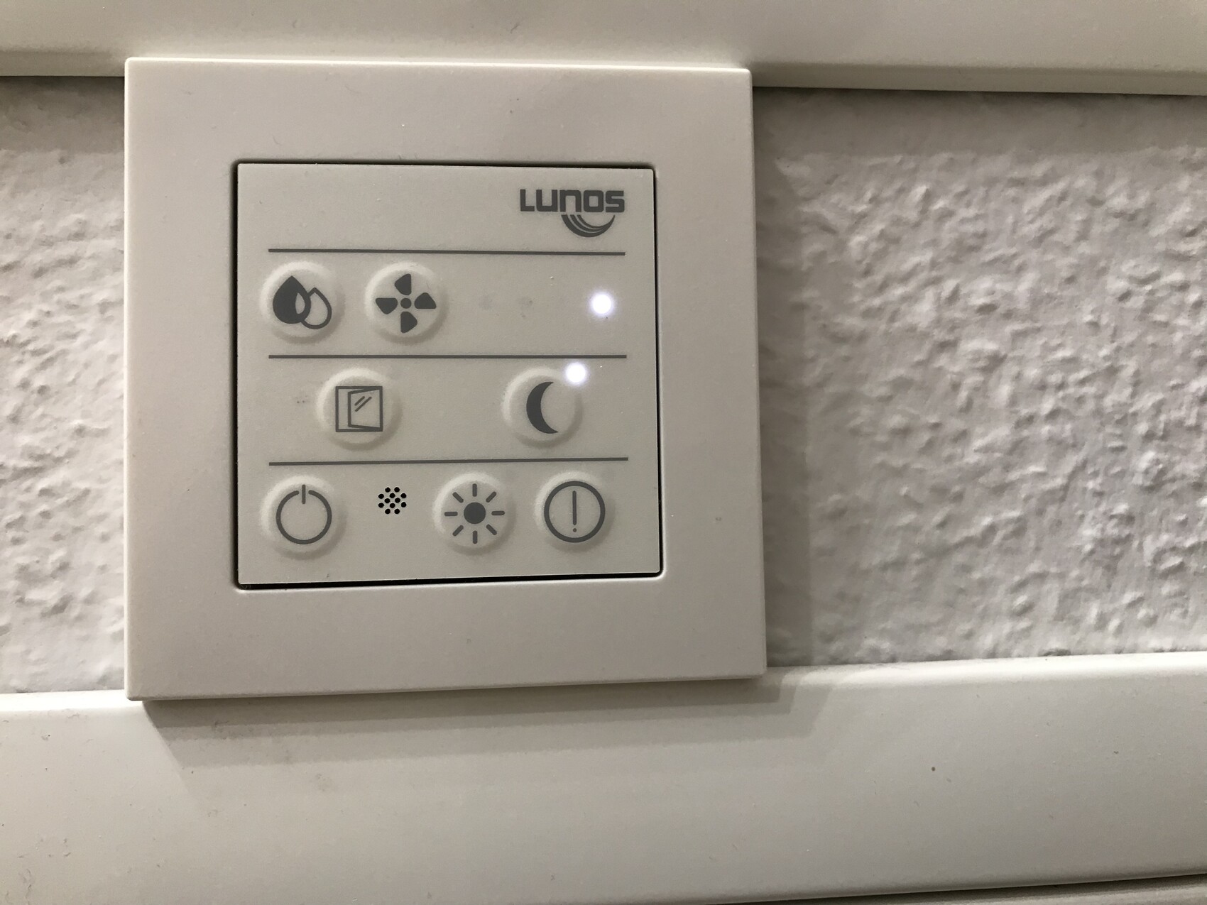 LUNOS-Lüftungssteuerung an weißer Wand mit Icons (Wasser, Ventilator, Nacht, Sonne).