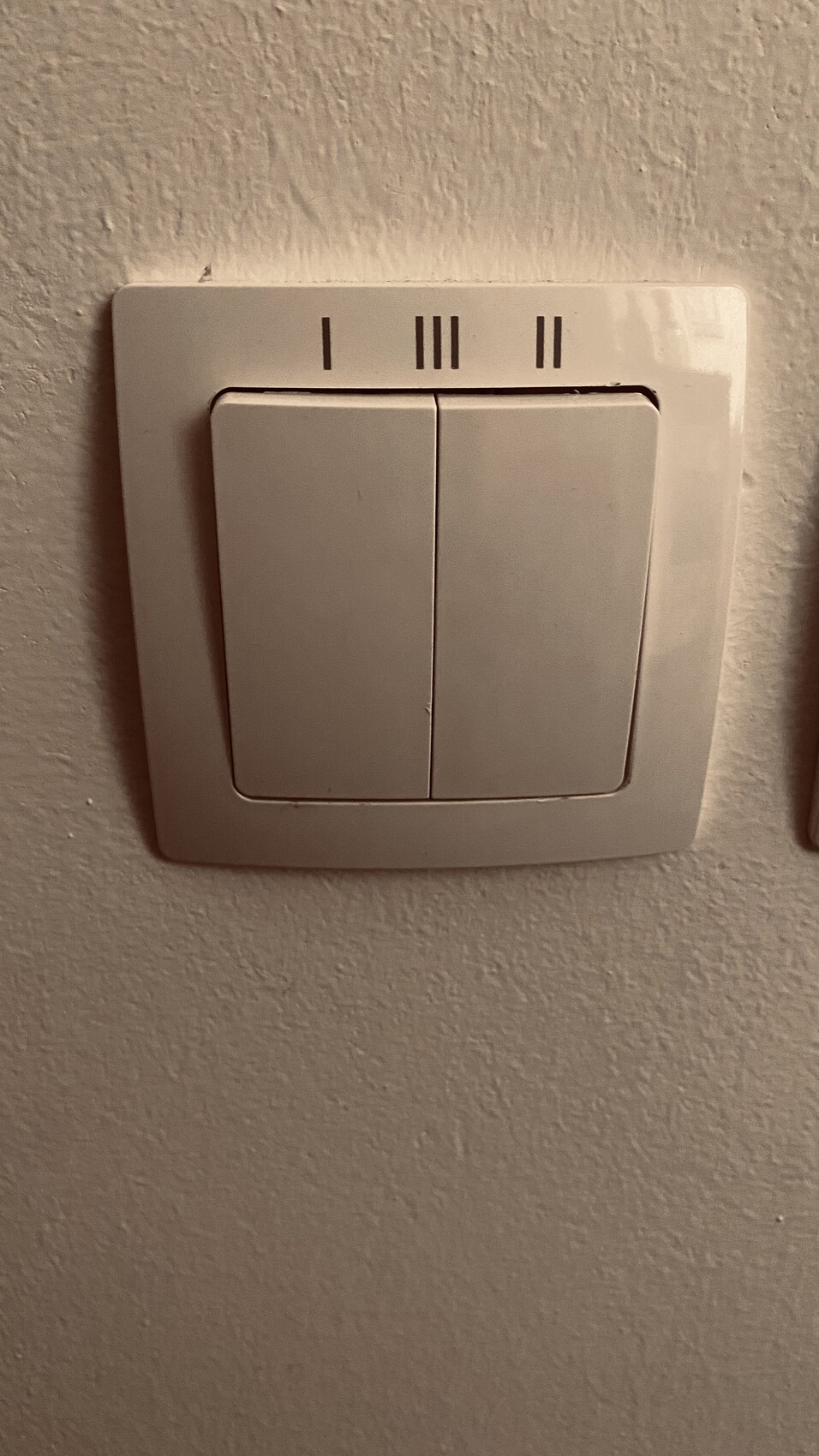 Doppelter Lichtschalter an weißer Wand mit zwei nebeneinanderliegenden Tastern.