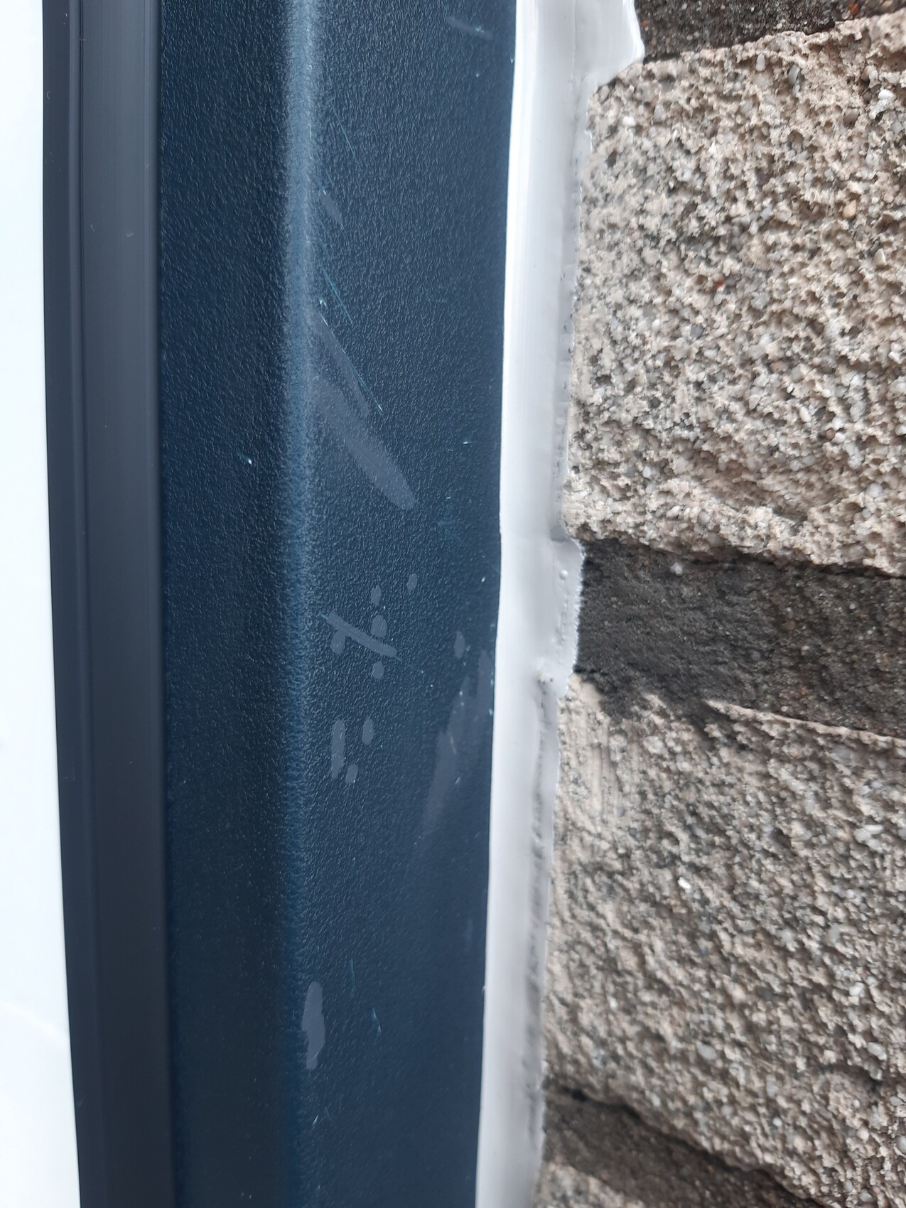 Nahaufnahme eines blauen Metallrahmens mit Dichtstoff neben rauem Steinmauerwerk.