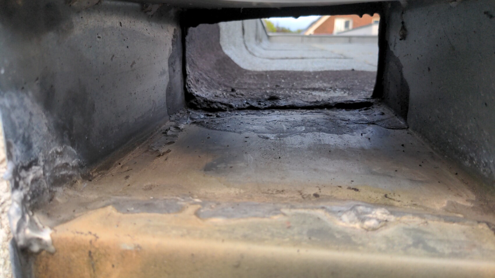 Dunkler, rauchverkrusteter rechteckiger Innenkanal; Blick durch Öffnung nach außen auf Dachziegeln.