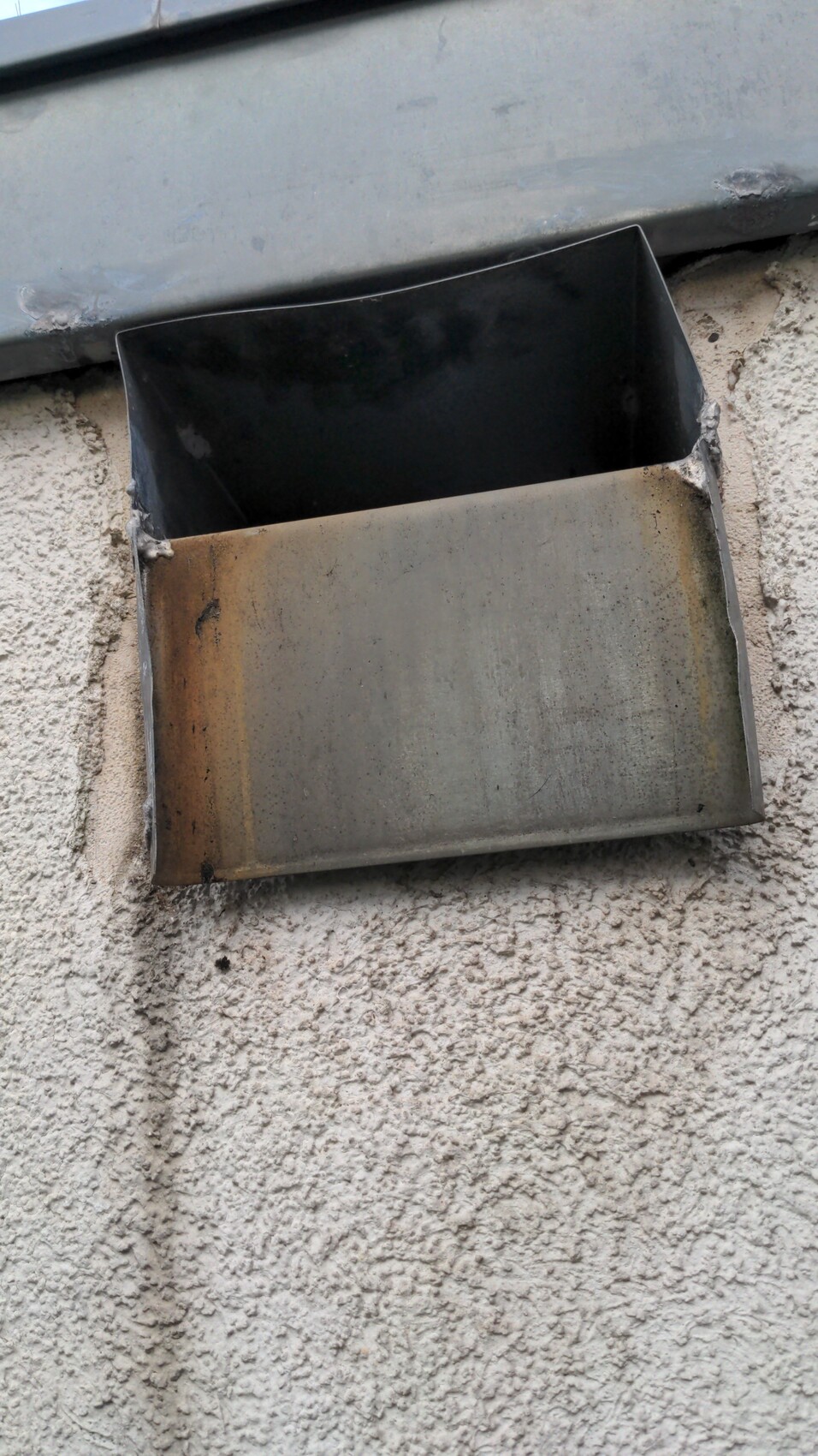 Rostige Metallbox in der Wand, offen nach vorne, auf rauer Putzoberfläche.