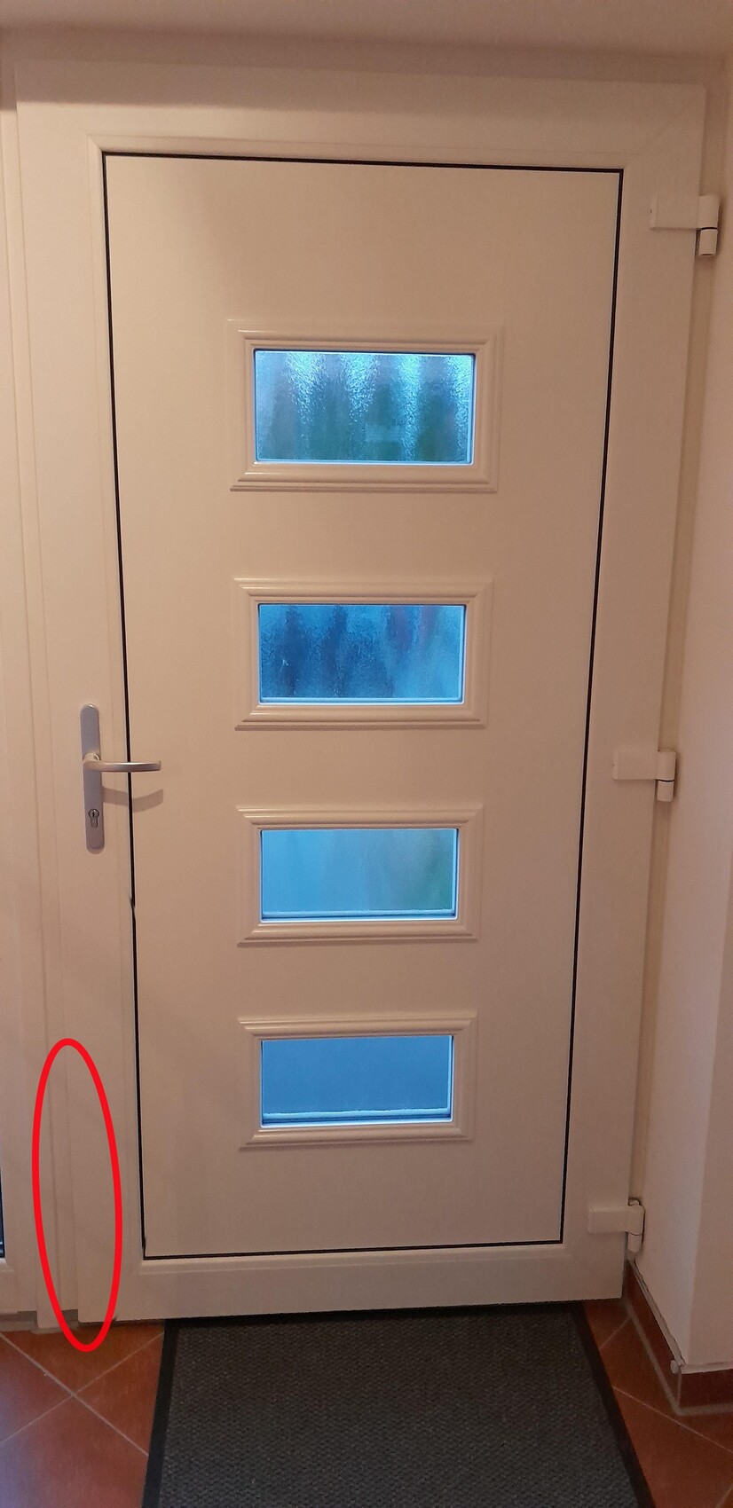 Weiße Tür mit vier vertikalen Glasfenstern, Türgriff links, Türrahmen und Fliesenboden davor.