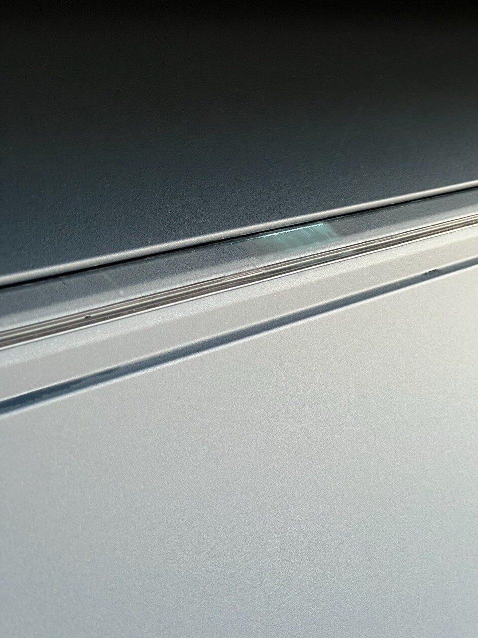 Nahaufnahme einer grauen Metalloberfläche mit kleinem grünem Kratzer an der Kante.