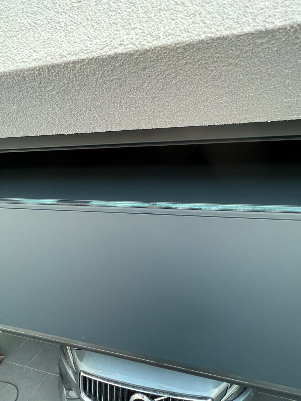 Vorderseite eines geparkten Autos mit Kühlergrill; darüber eine raue Wand.