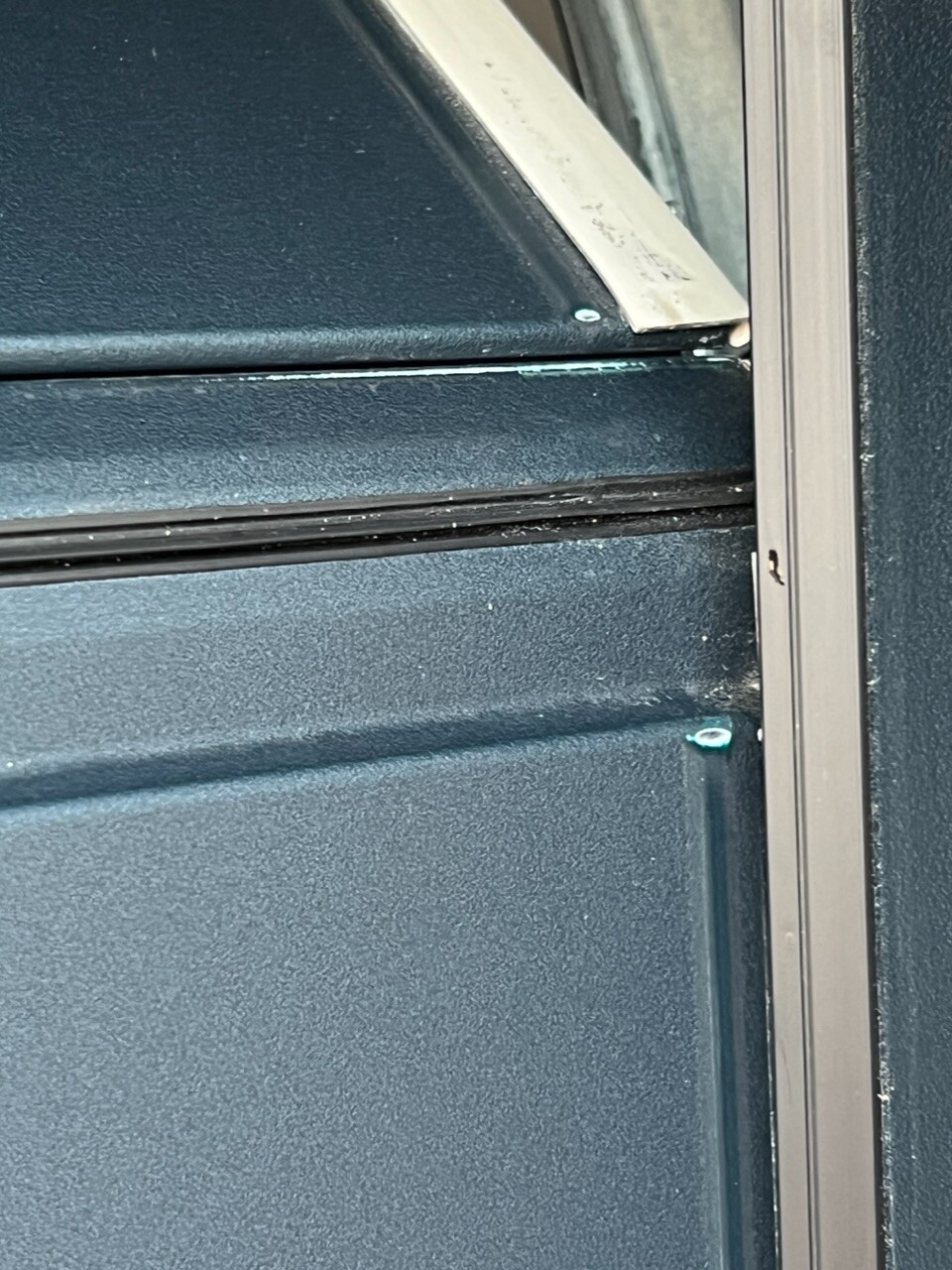 Nahaufnahme einer dunklen Metalloberfläche mit diagonalem silbernem Streifen und Gummidichtung.