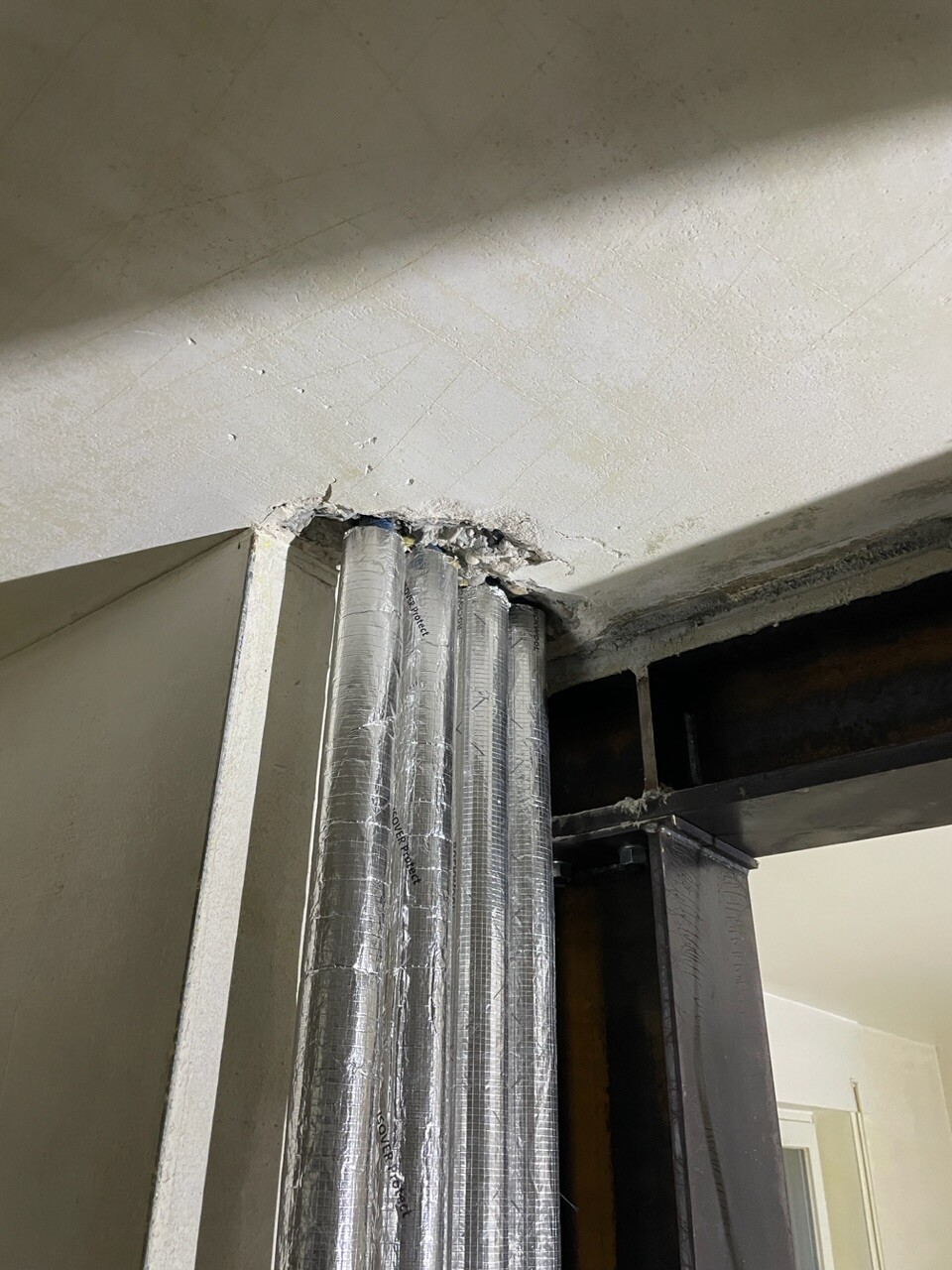 Mehrere silberne, isolierte Lüftungsrohre verlaufen durch eine Wandöffnung im Rohbau.