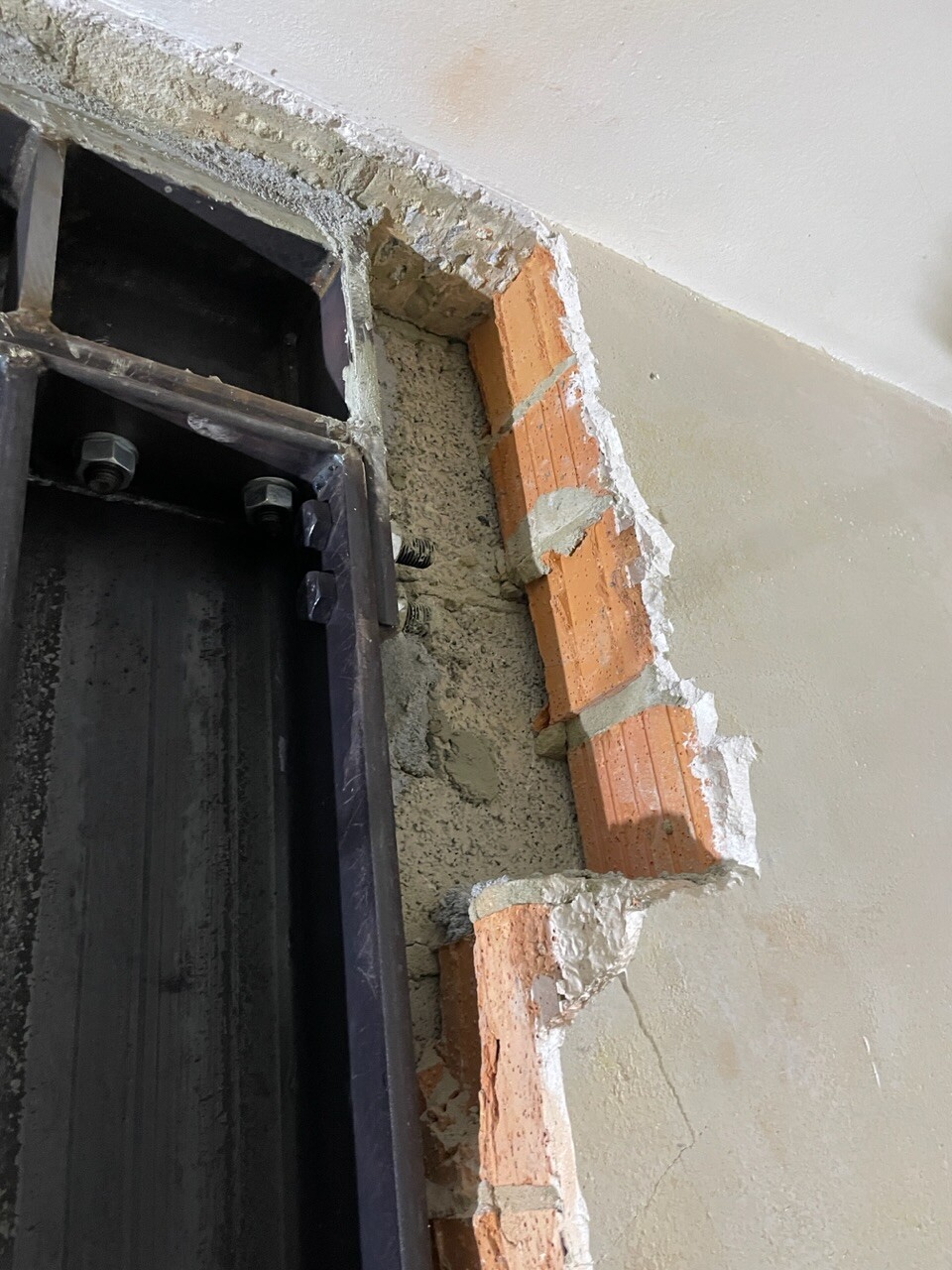 Beschädigte Wand neben Türrahmen mit freigelegten Ziegeln und Mörtel.