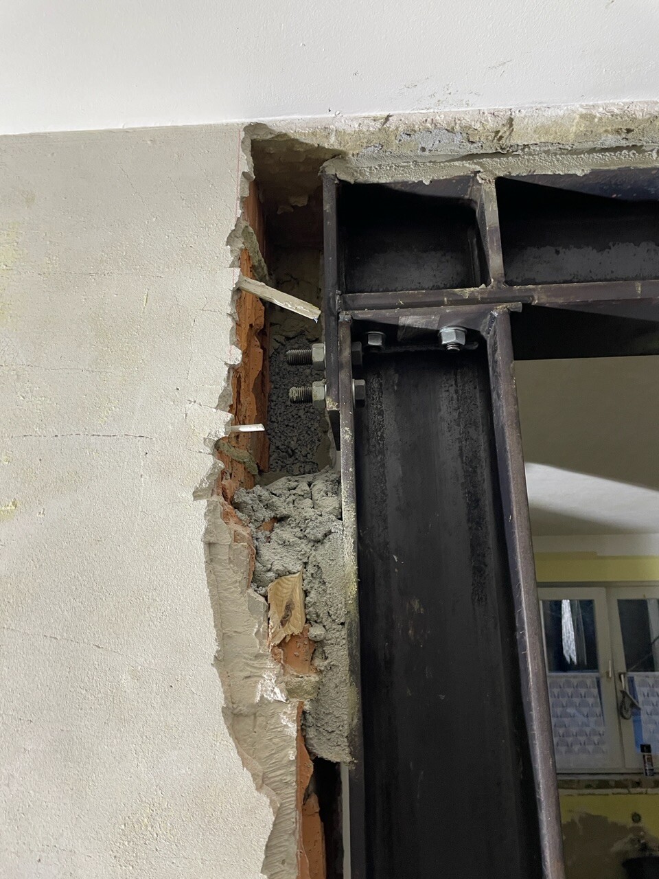 Beschädigte Wandöffnung mit Stahlrahmen, Bolzen, Zementmörtel und Bruchsteinmauer.