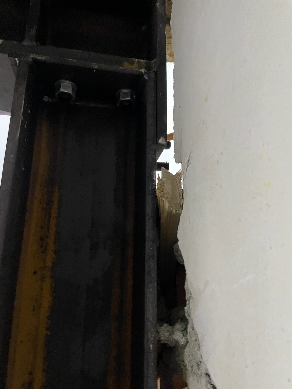 Nahaufnahme eines schwarzen Metallrahmens mit Bolzen, daneben bröckelnde Putzwand.