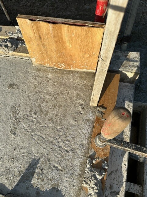 Baustelle: Betonboden, Holzplatten und Schraubendreher im Beton sichtbar.