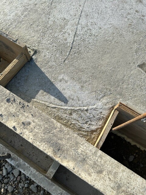 Baustellenszene: Betonboden mit Holz-Schalungen an beiden Seiten und Kies am Rand.