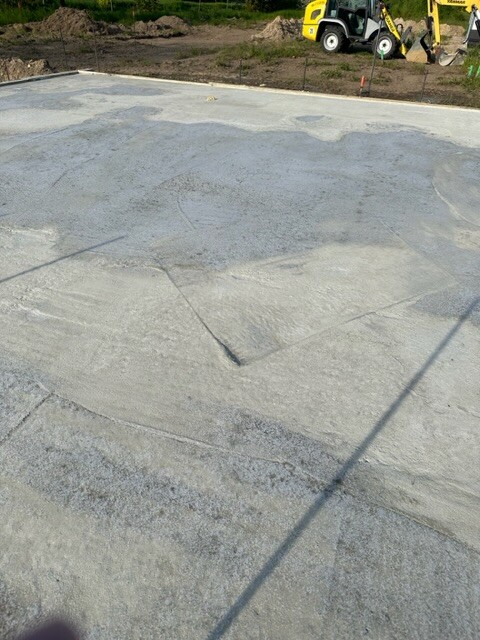 Große Betonfläche auf einer Baustelle, im Hintergrund ein gelbes Baufahrzeug.