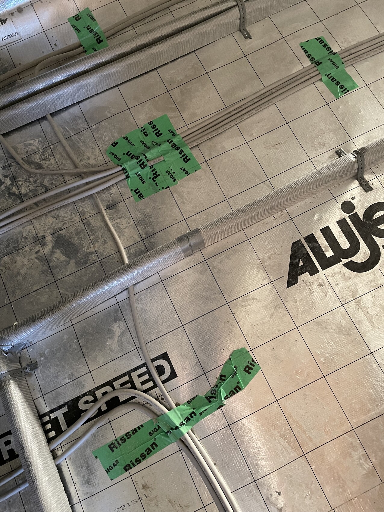 Isolierte Metallkanäle und Kabel auf Baustellenfläche; grüne Klebebänder sichtbar